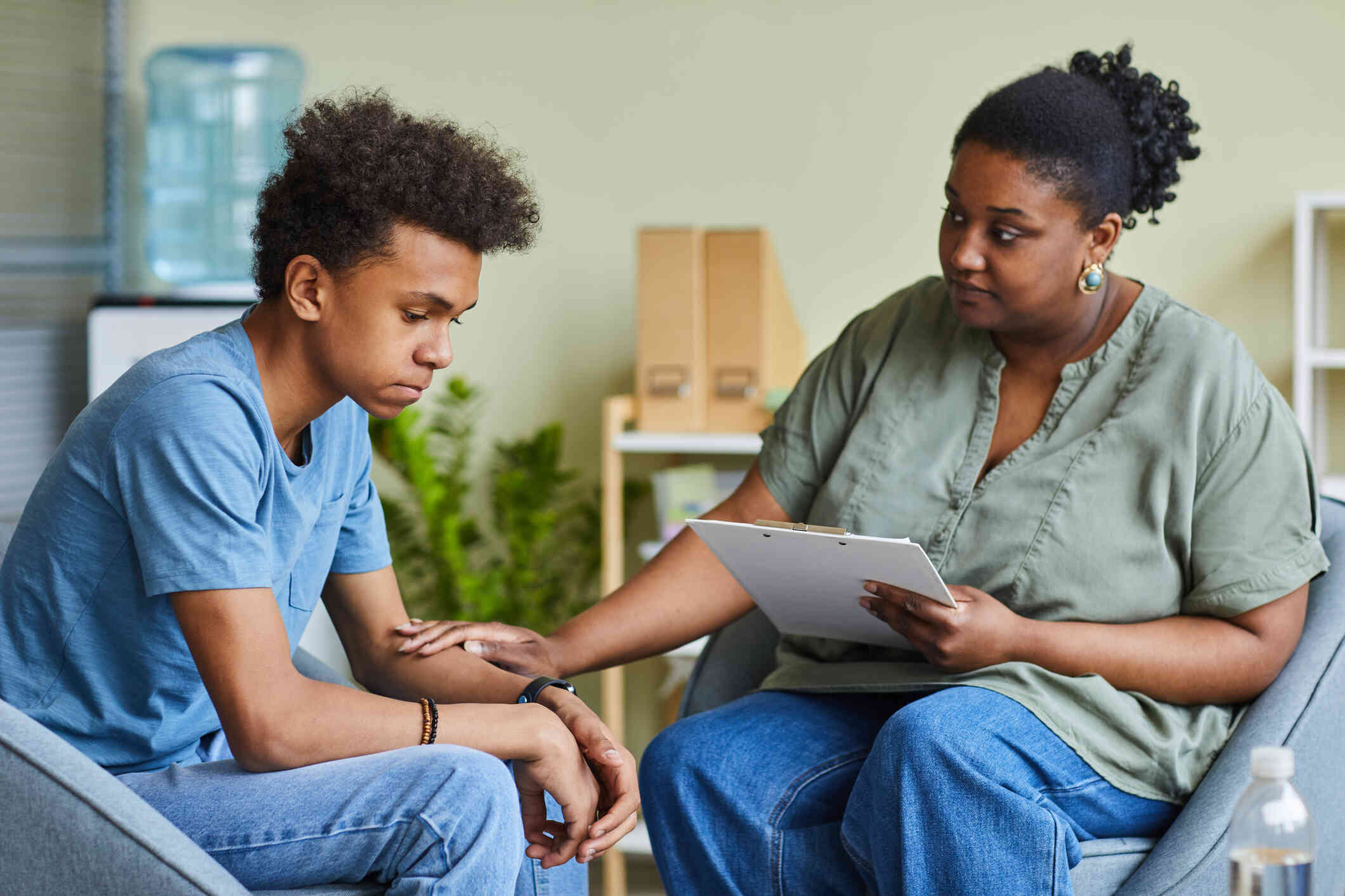 A female therapist rests her hand on her male patients arms comfortingly during a therapy session.