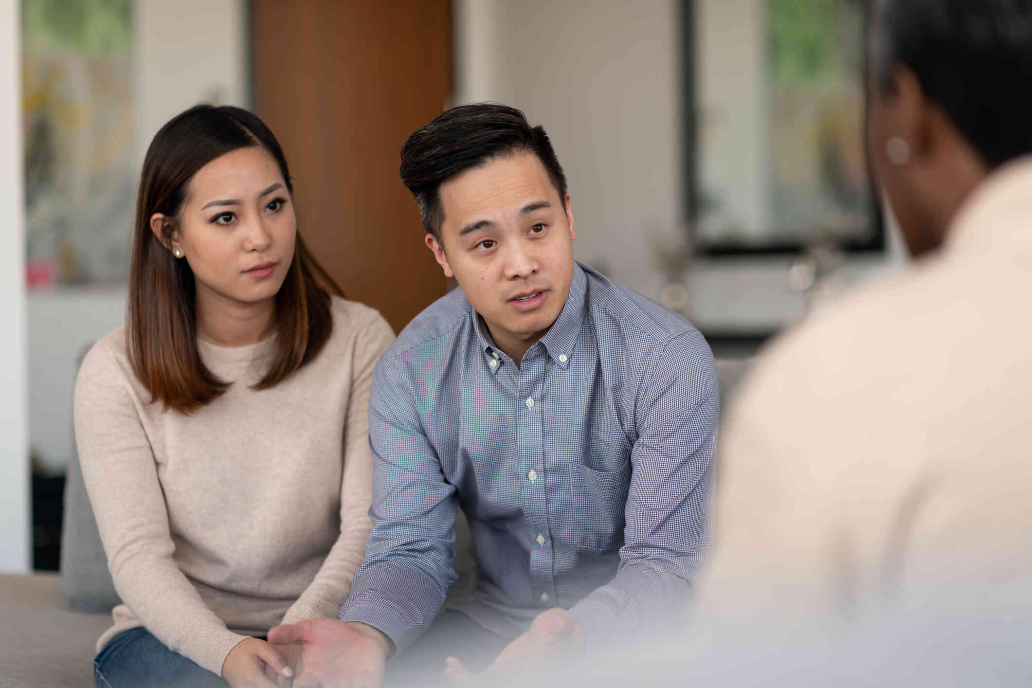 A male and female couple sit next to each other on a couch while talking to the therapist sitting across from them.