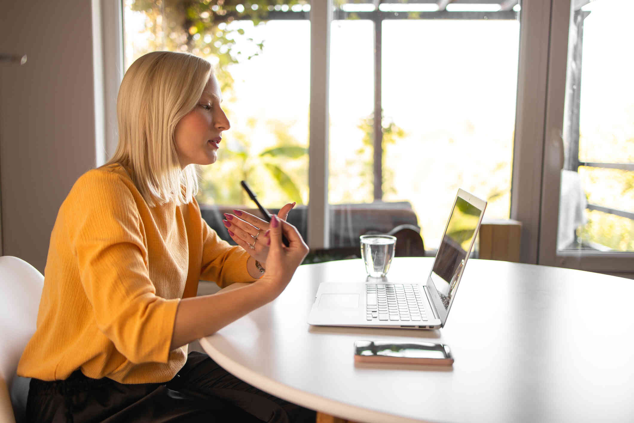 A woman in a yellow top gestures while on a video call through her laptop.