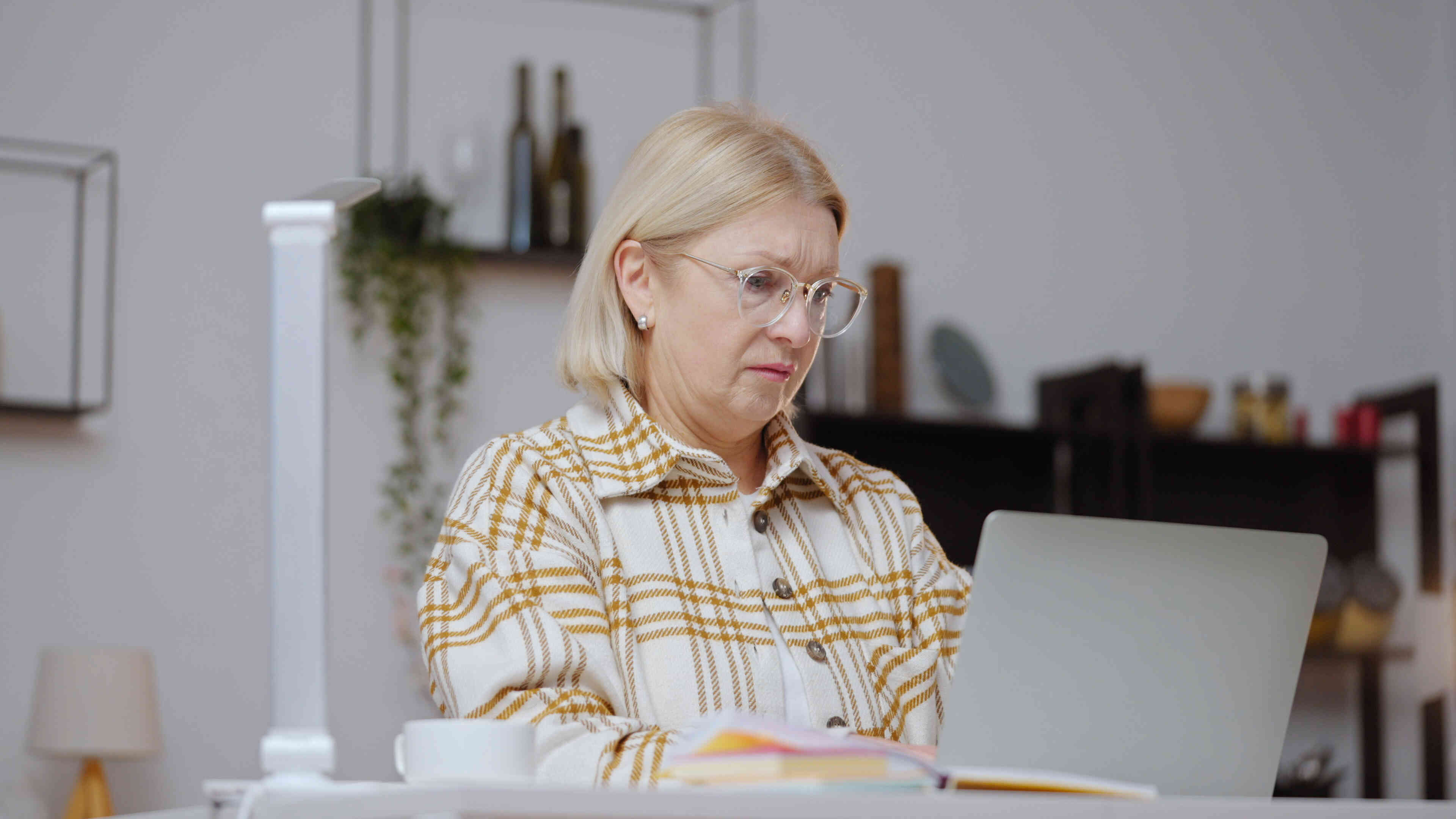 An older woman seated at a table is fully focused while typing on her laptop.