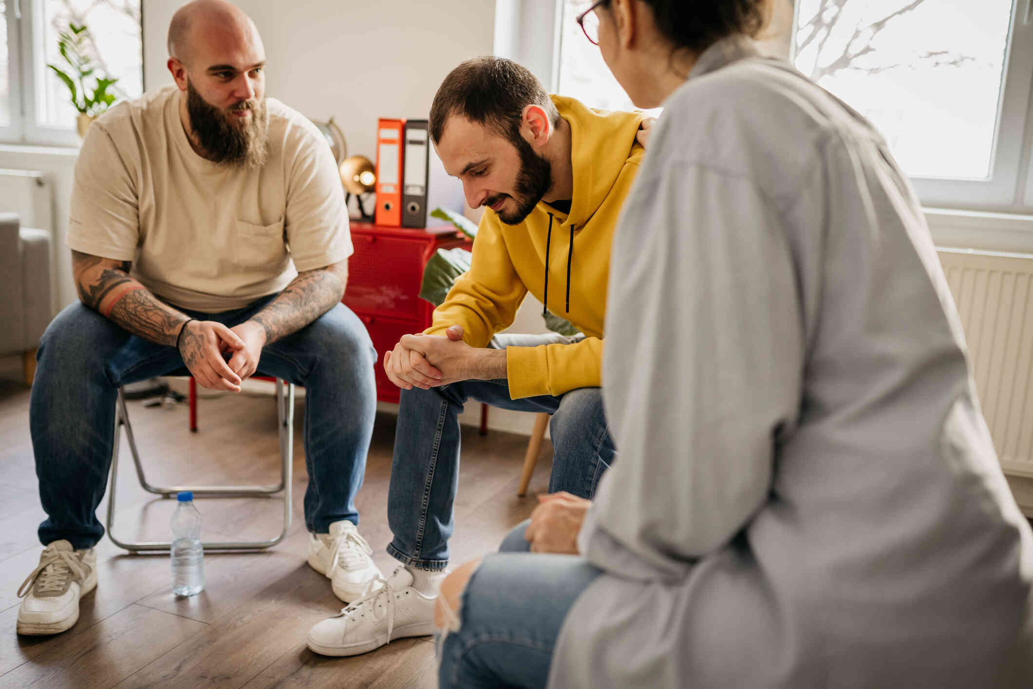 A close up of three adults sitting next to each toher during a support group therapy session.