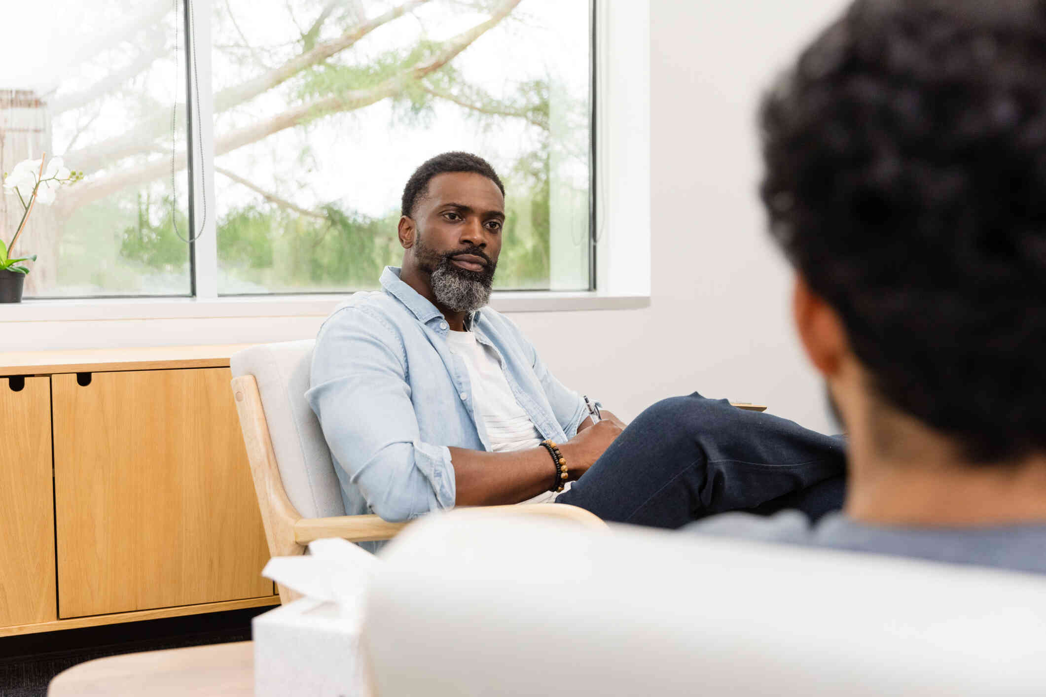 A male therapist listens intently to the male patient sitting across from him during a therapy session.