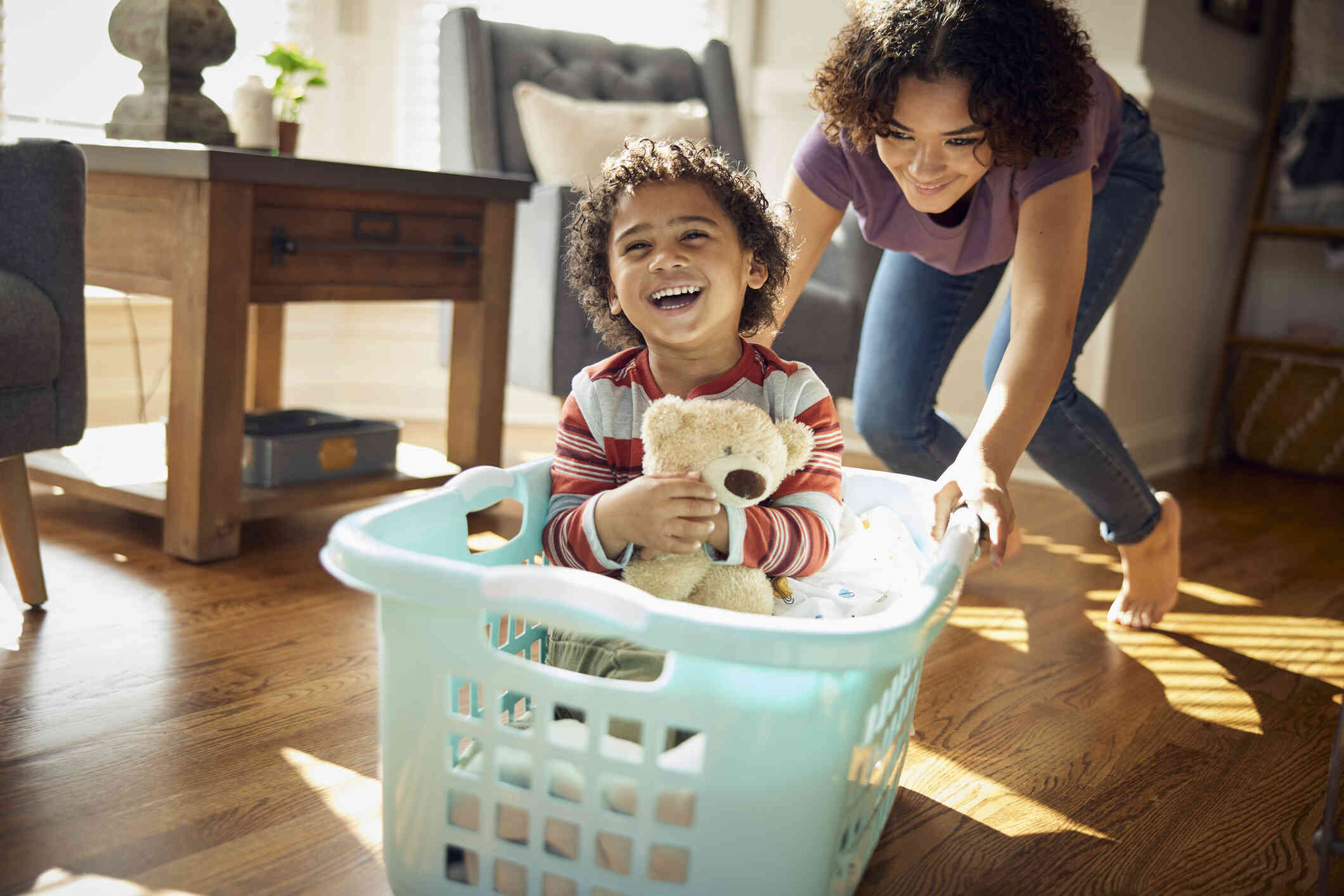 A little boy sits in a laundry basket and laughs as his mother pushed him around playfully across the floor.