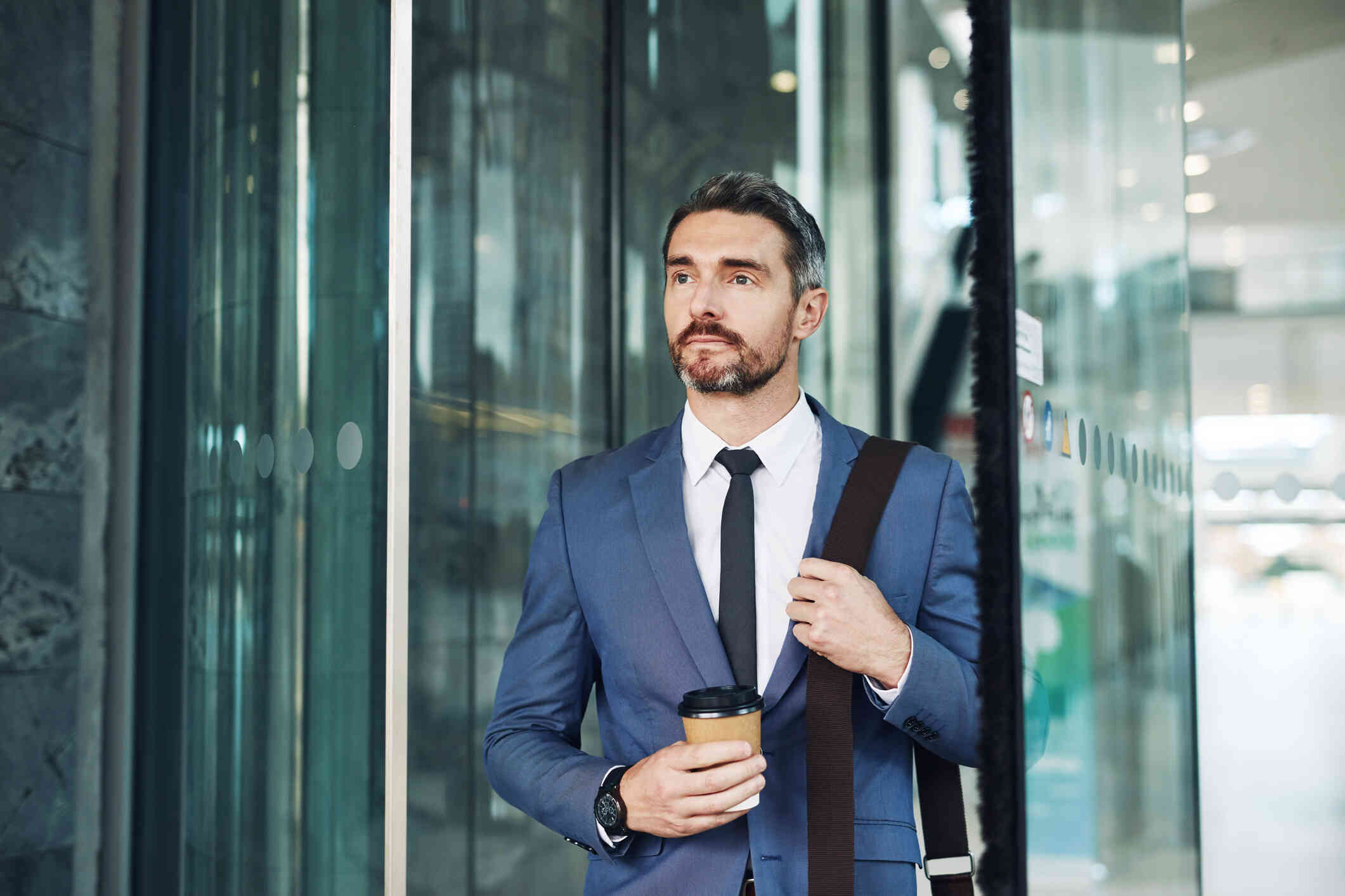 A man stands outside a building, holding his coffee.