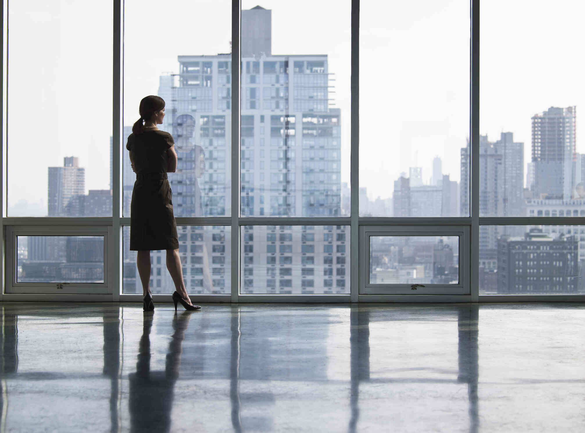 A young woman inside an office building facing away, looking out a window.