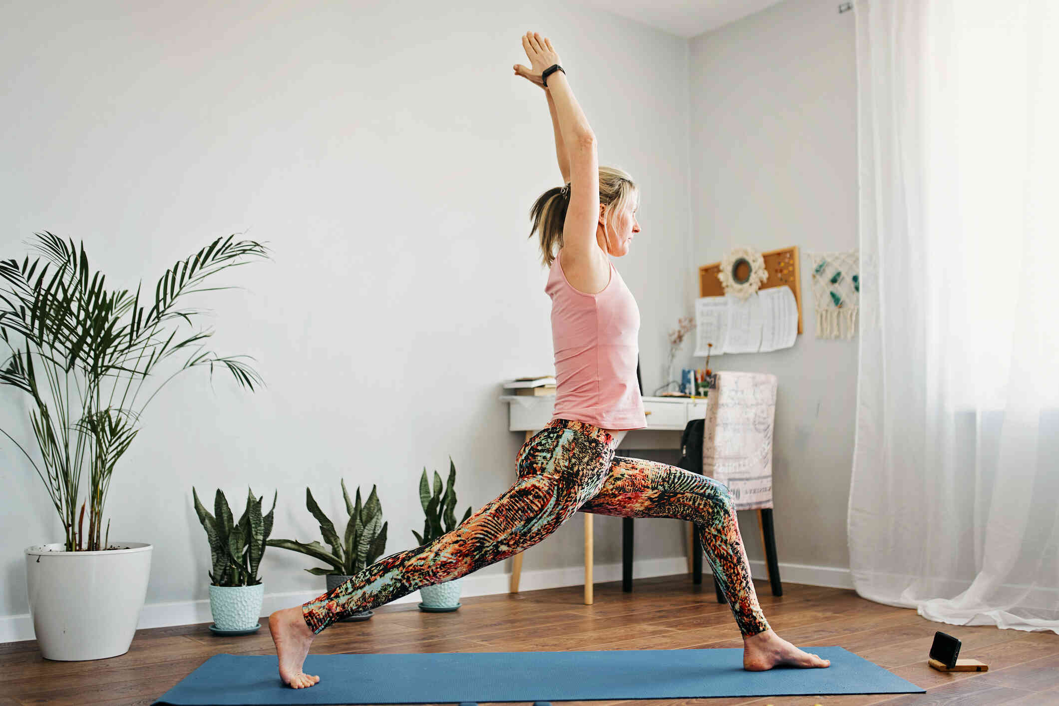 A woman stretches in a yoga pose while standing on a yoga mat in her room.