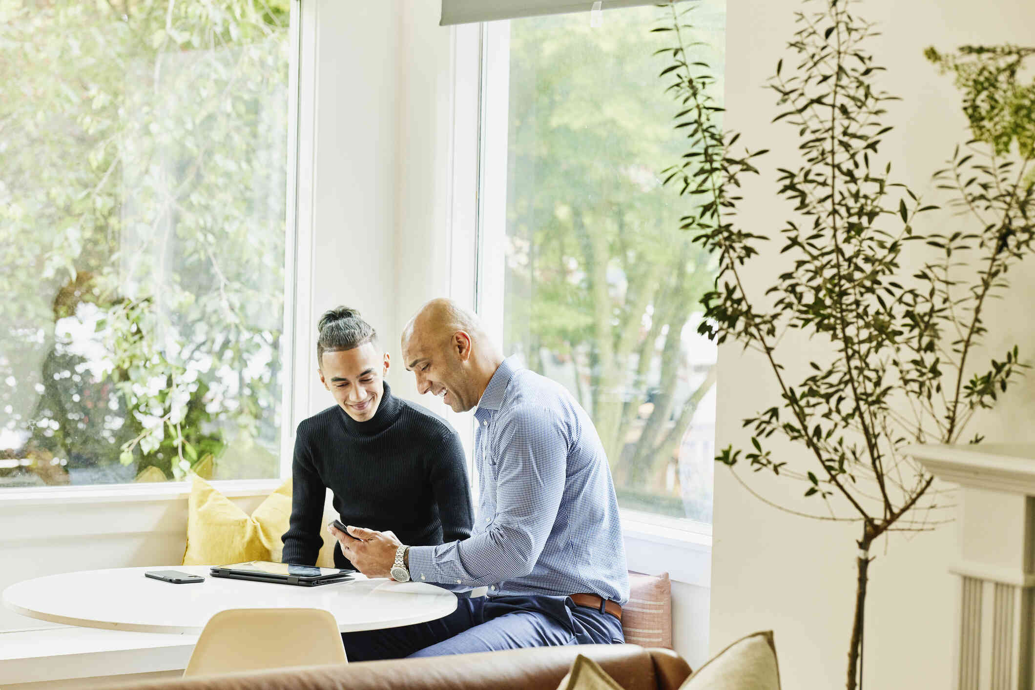 A teenage boy and his dad sit at a table, both looking at the phone screen.