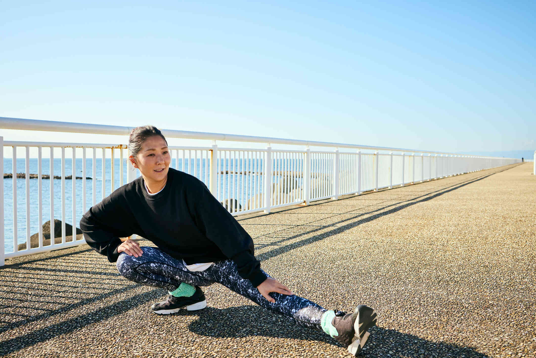 A woman in workout clothes stretches outside on a sunny day before going for a run.