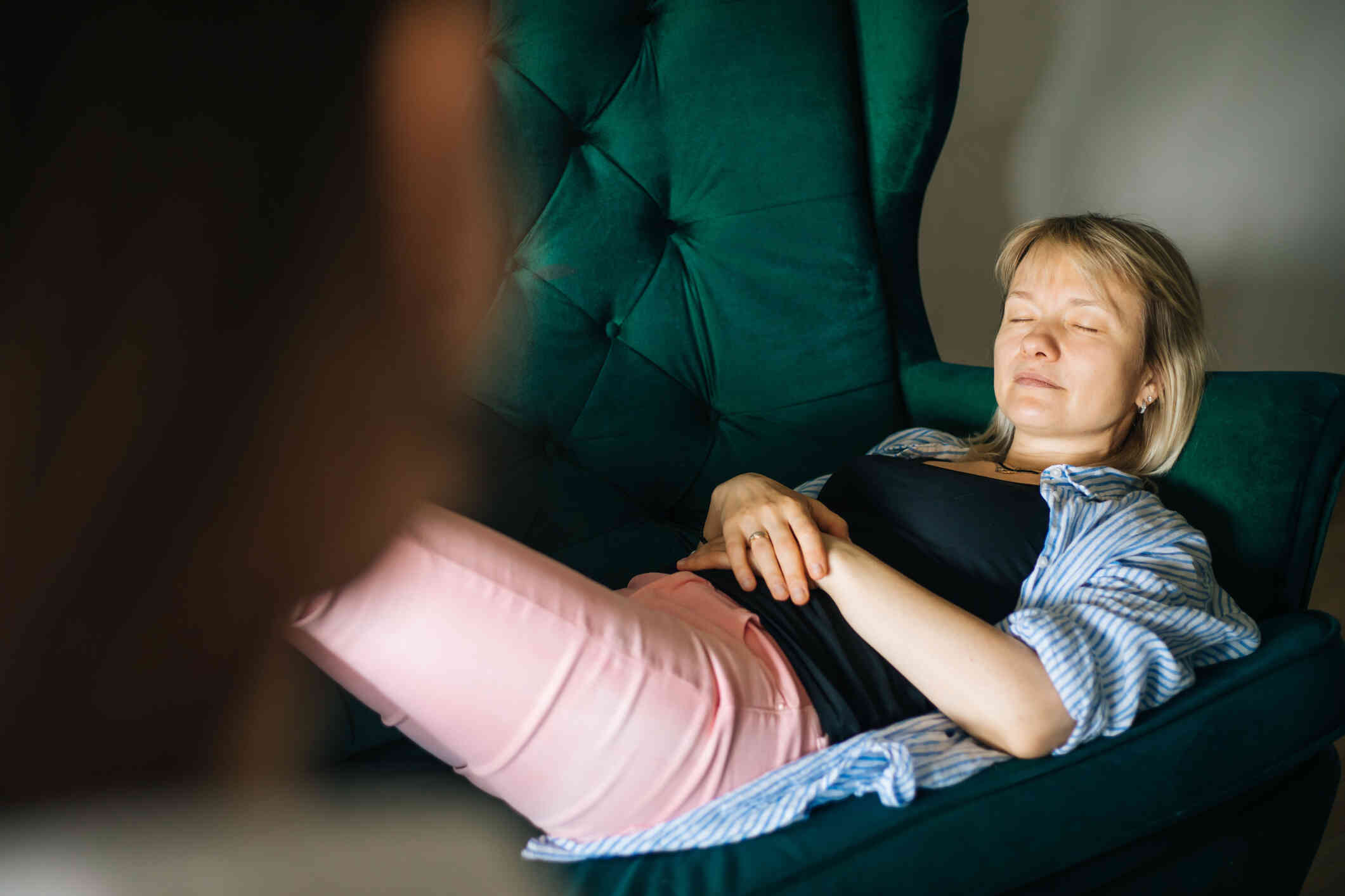 A woman in a blue striped shirt lies on a green couch while closing her eyes