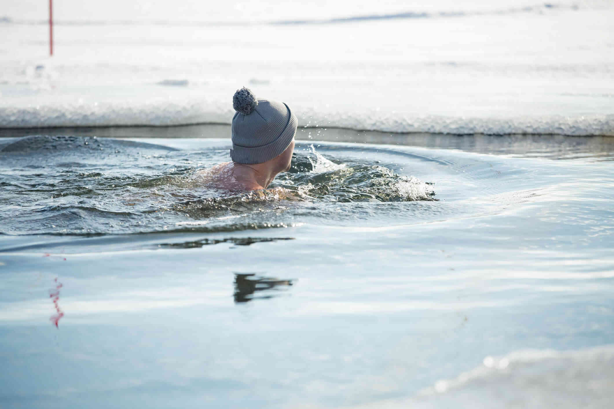 A man in a beanie swims around in an outdoor body of water which has ice in the background.