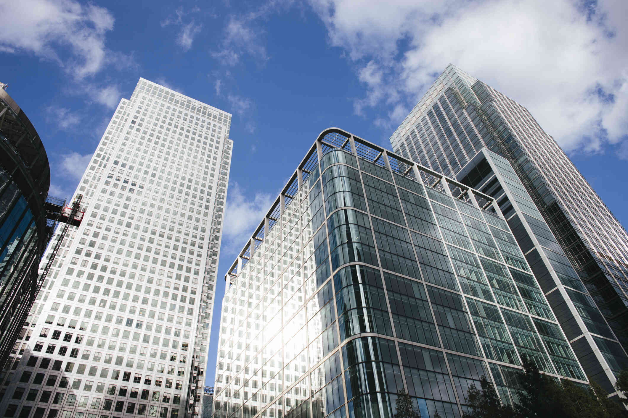 A glass office building with many windows in a city stands tall on a nice day and clouds are above