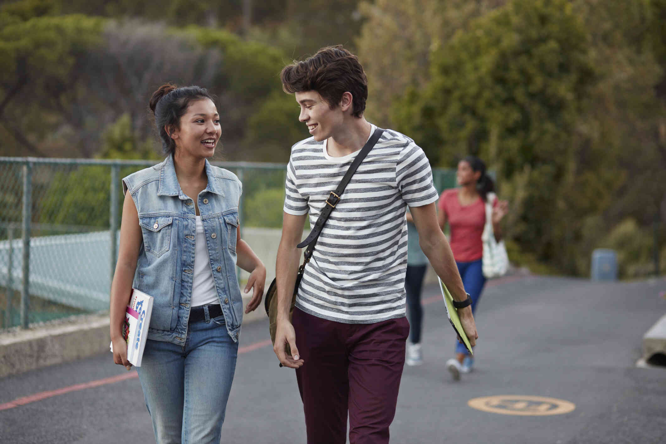 A woman and her male friend walk side by side outside on a sunny day while smiling and chatting.