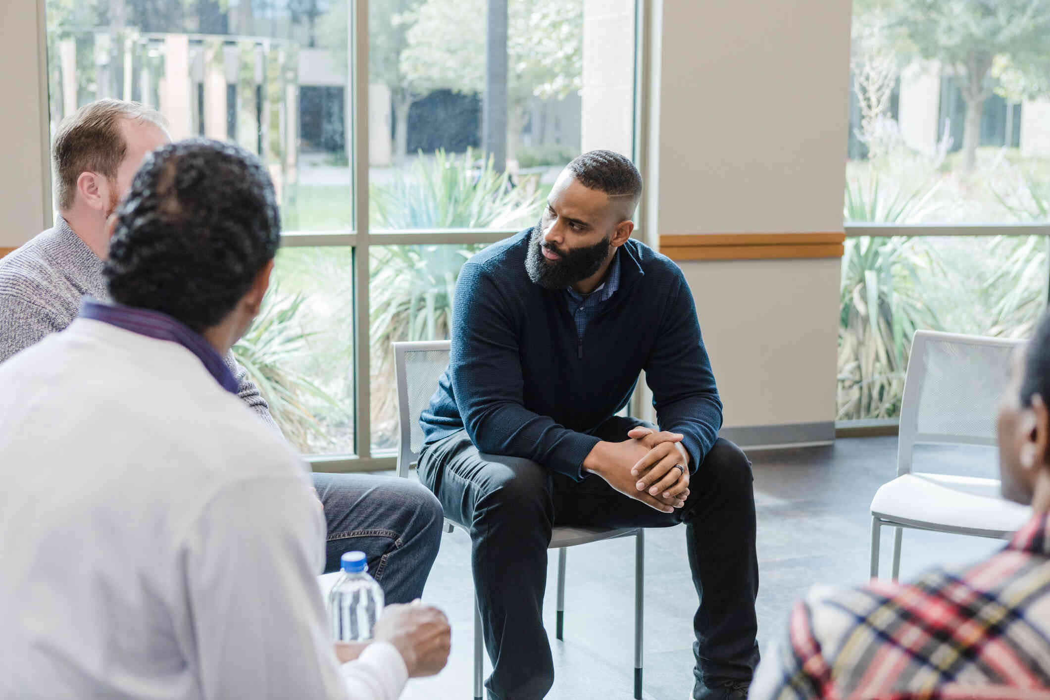 A group of adult men sit together in a circle during a group therapy session.