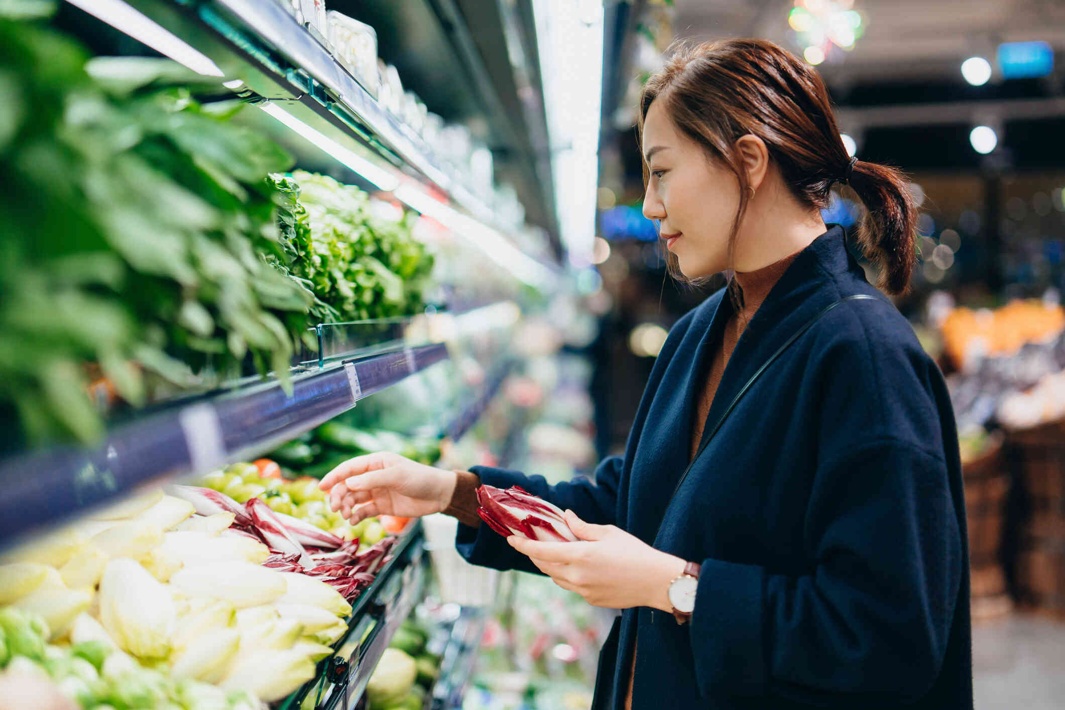 A woman in a blue sweater goes grocery shopping in the produce section  section of the grocery store.