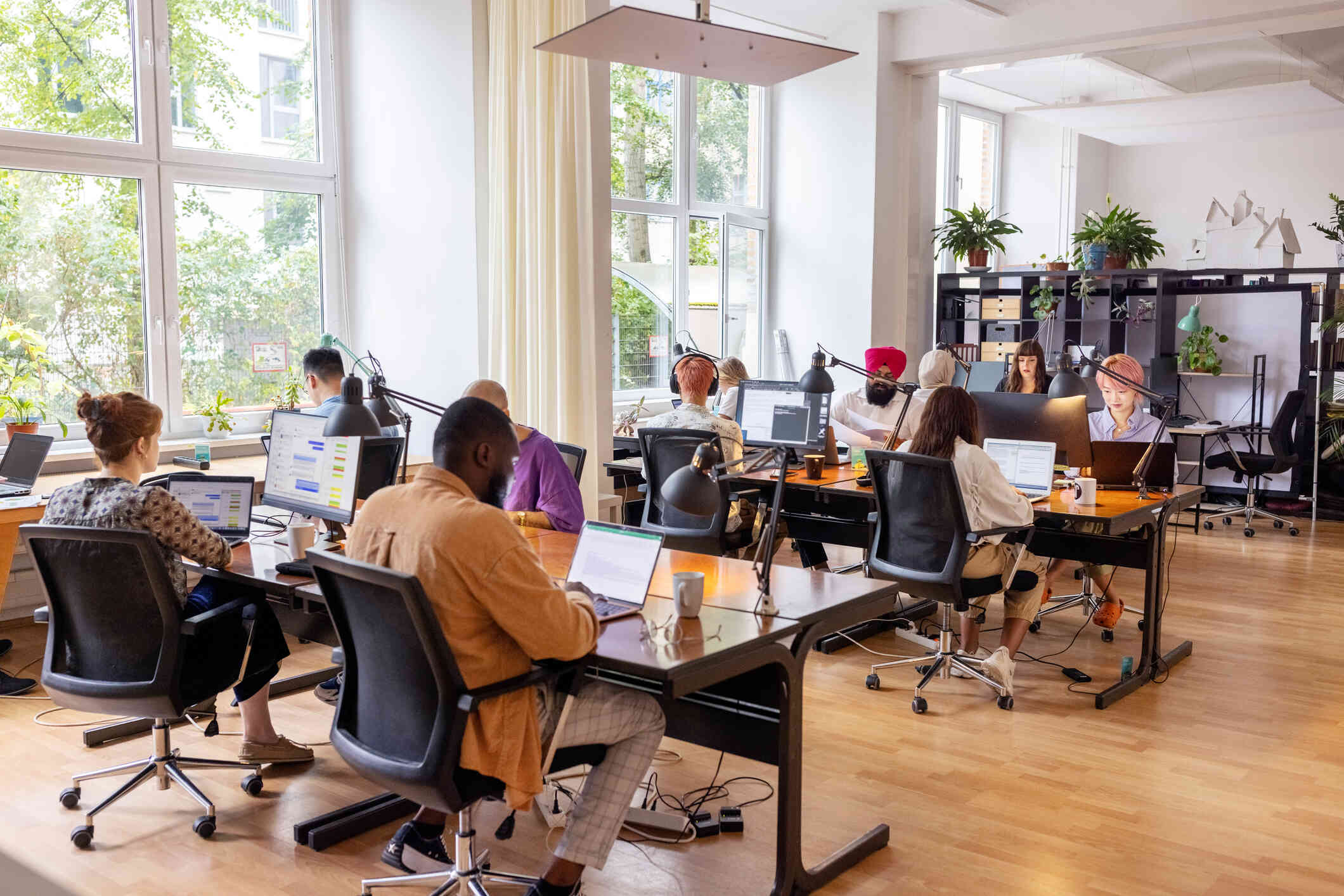 A group of people work together in an open modern office space while all looking down at their computer