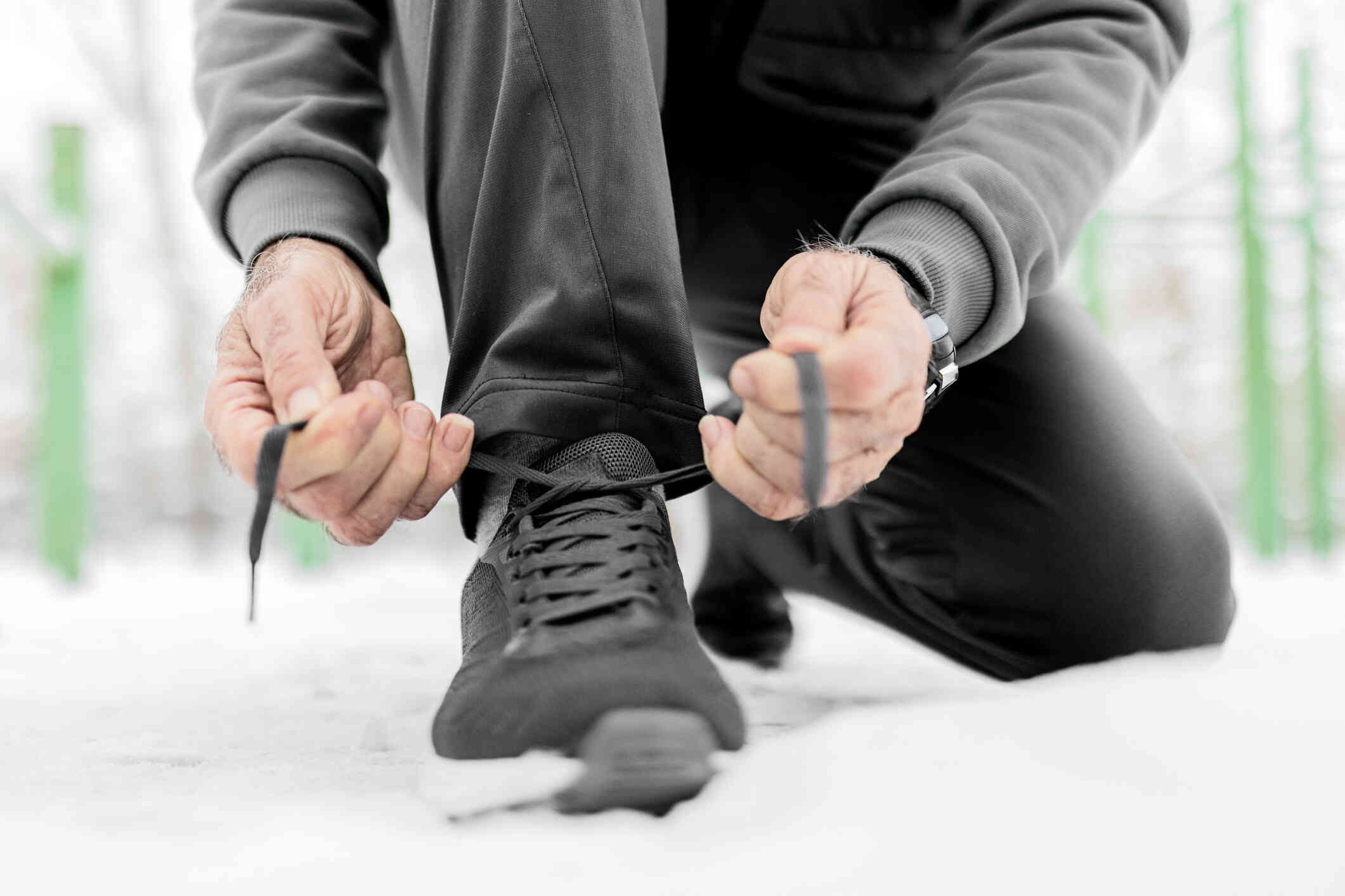 A close up of a man kneeling down as he ties his tennis shoe lace.