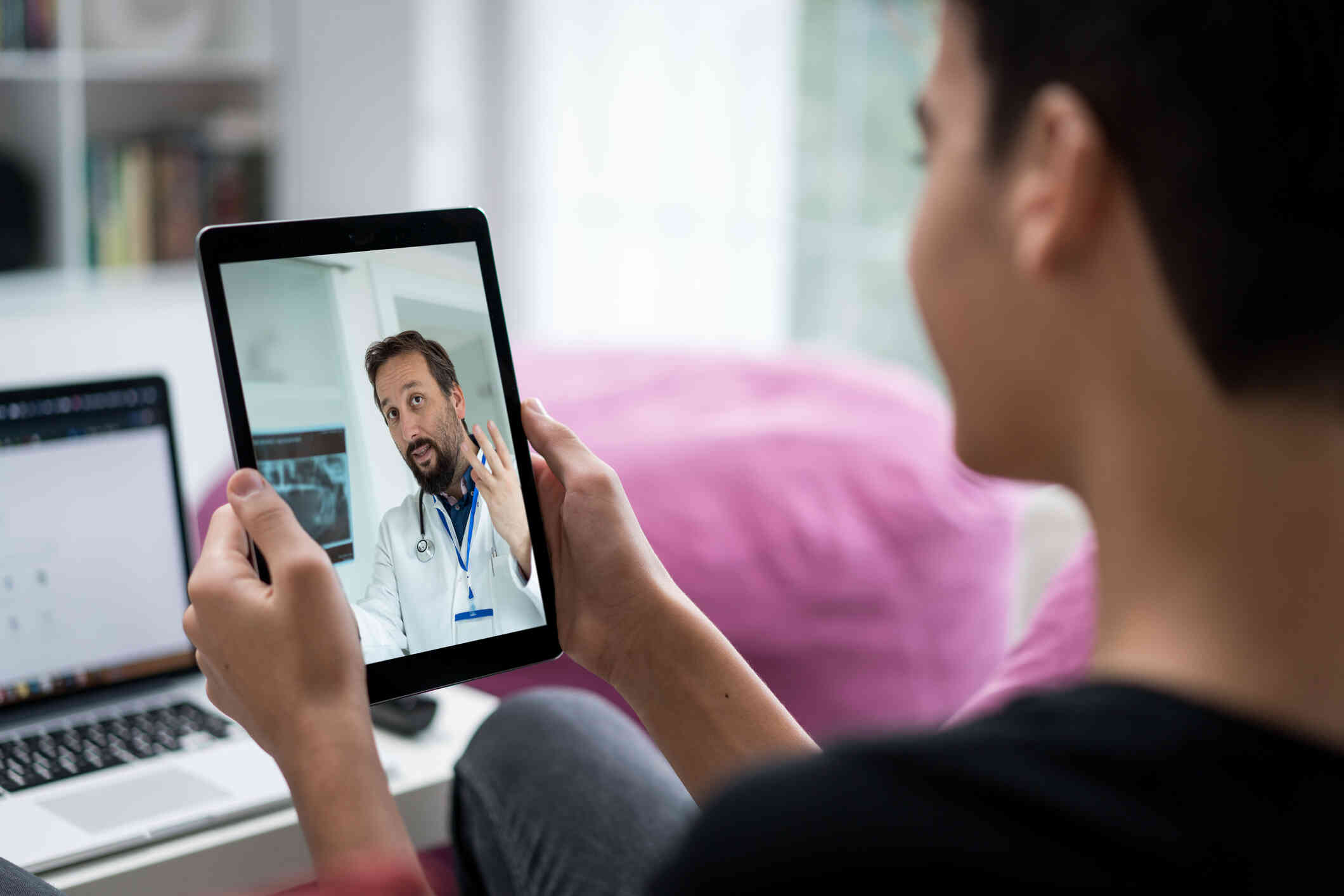A close up of a woman holding a tablet in her hand while talking to the  male doctor on the screen during a telehealth call.