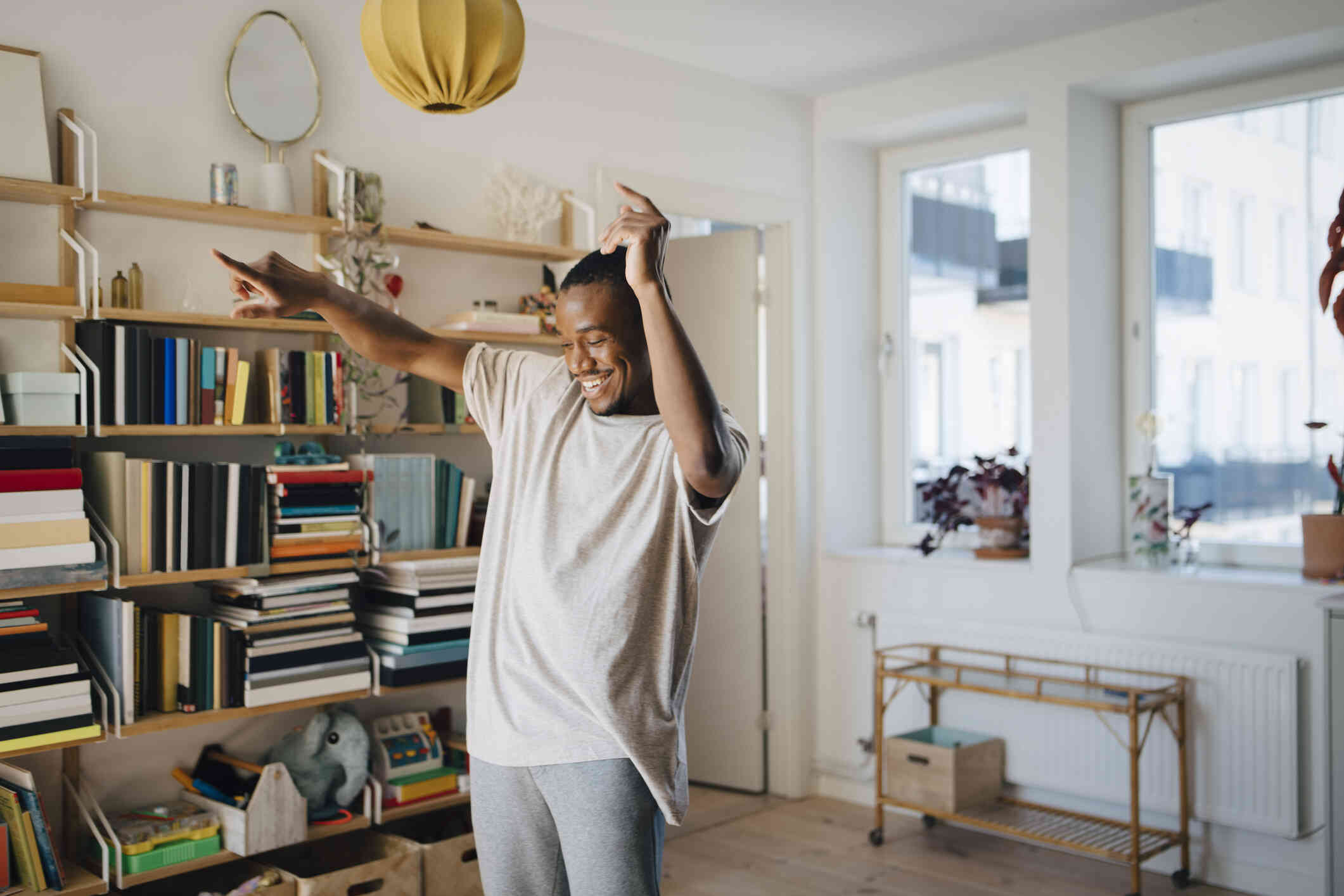 A man in a tan shirt dances in his home while smiling.