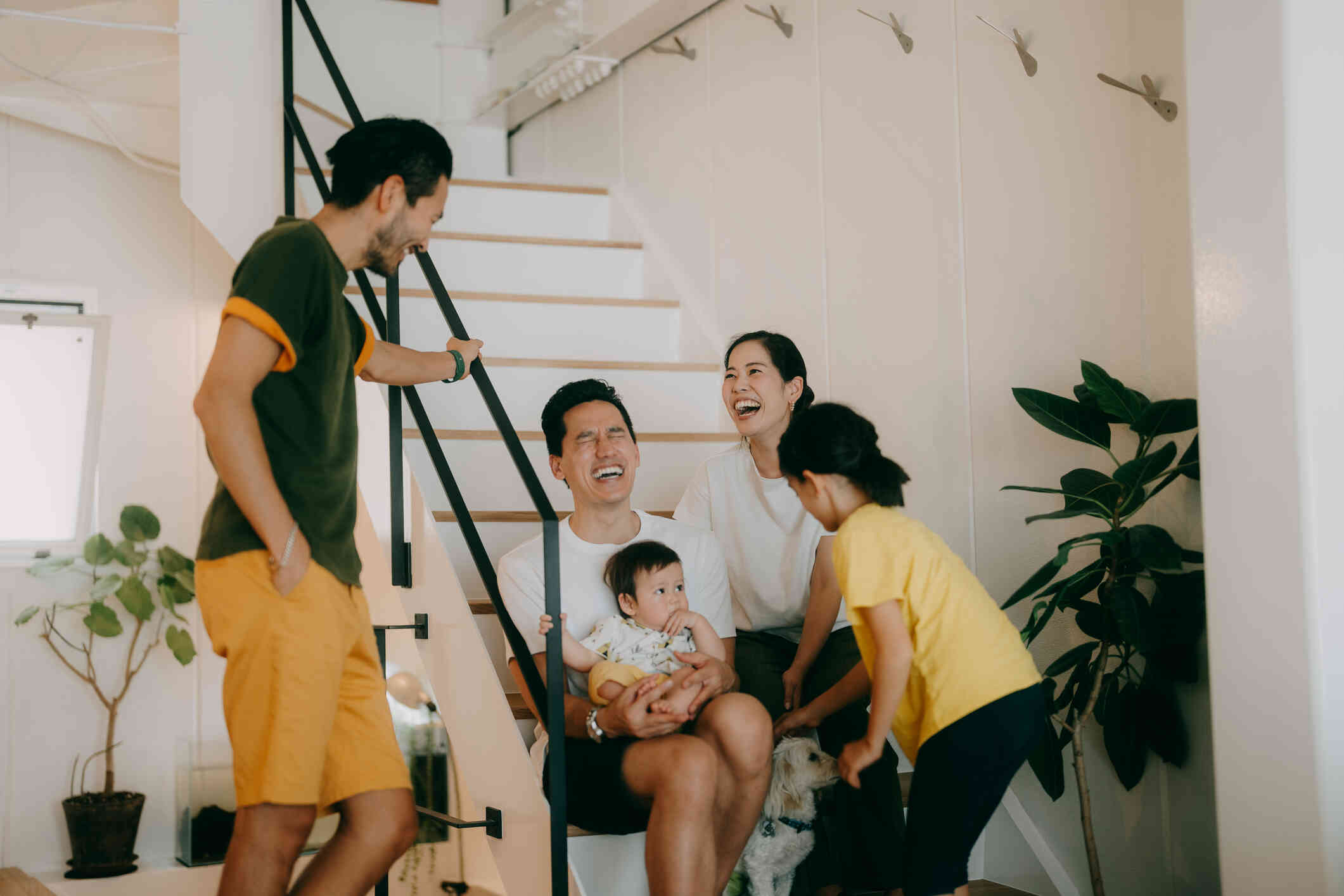 A family of five hang out together around the staircase in their home while laughing together.