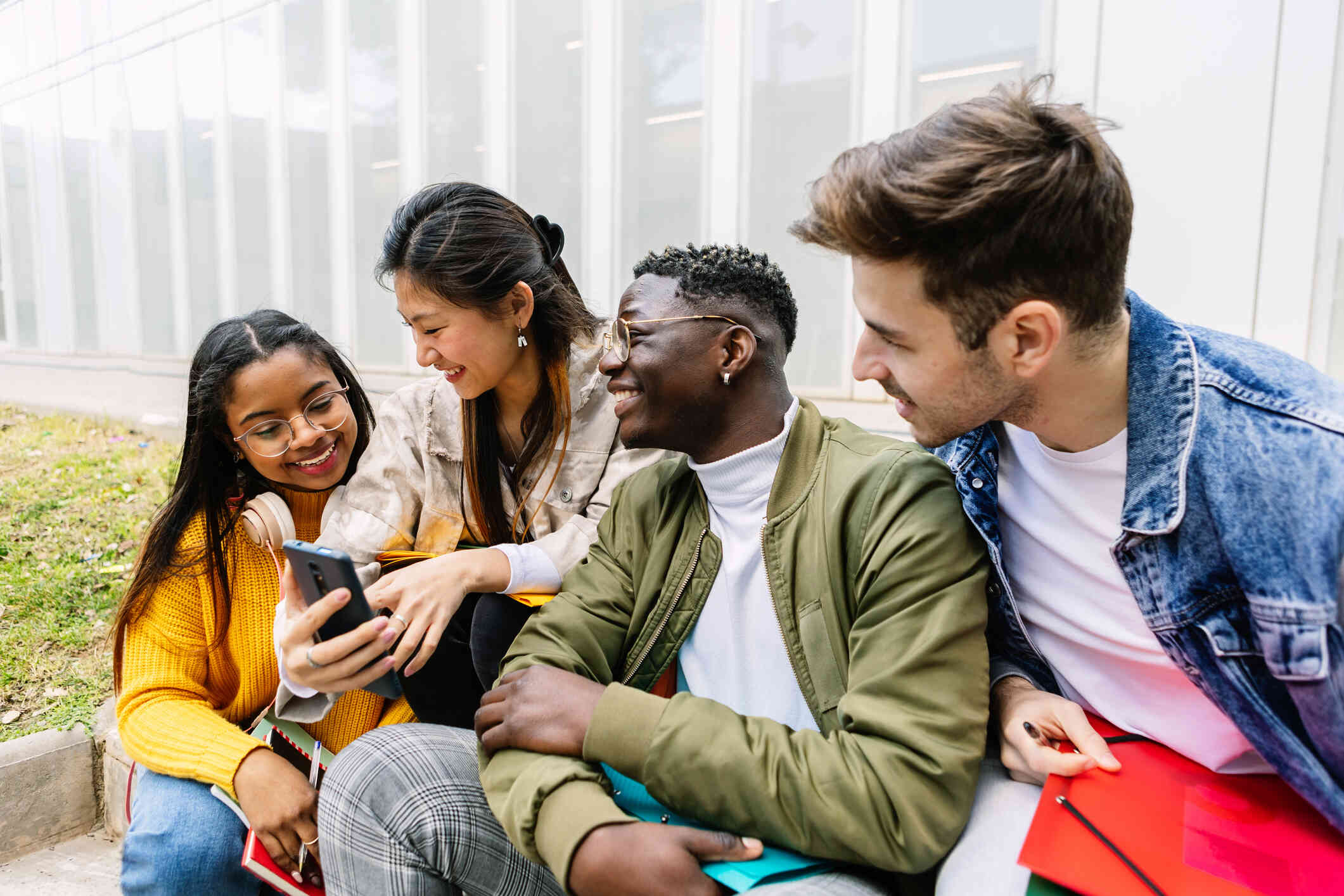 Four adult friends sit close together while smiling and looking at a phone screen.