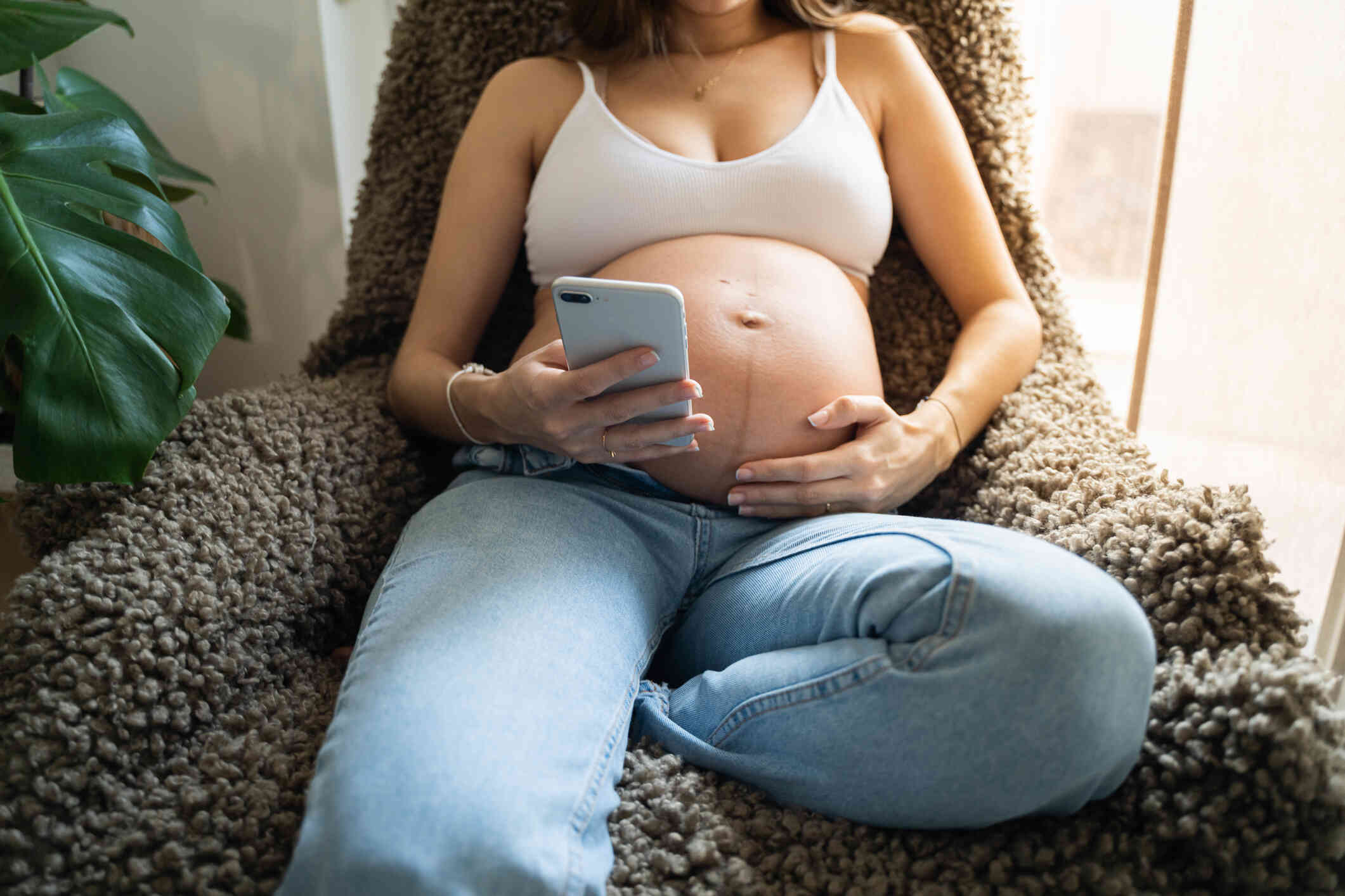 A close up of a pregnant woman as she reclines in a chair and looks at the phone in her hand.