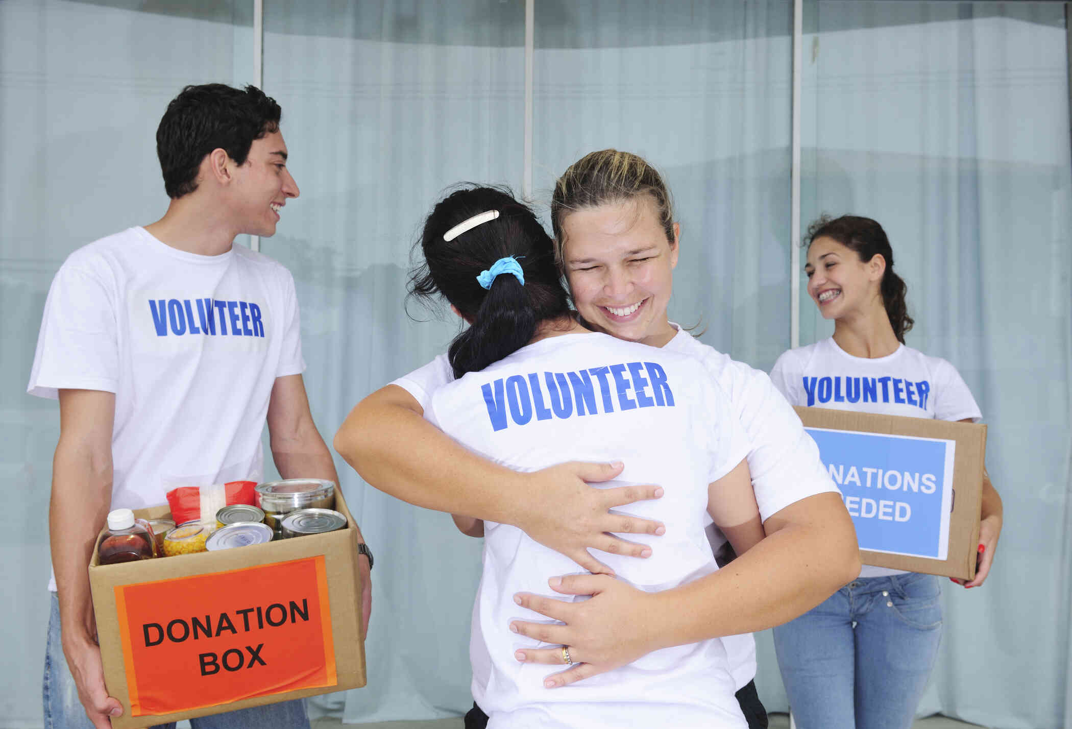 A young woman smiles and hugs another woman wearing a shirt which says 