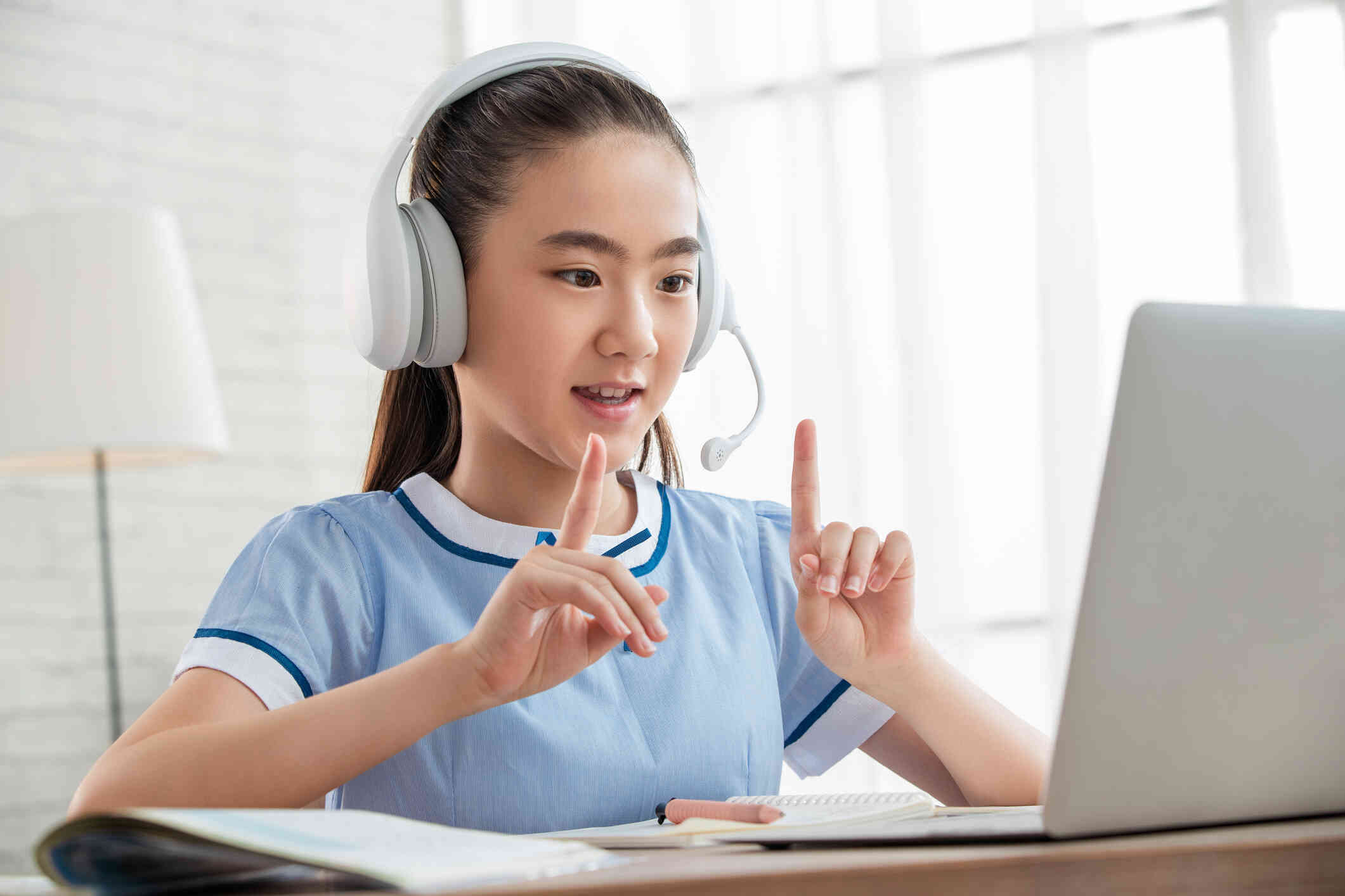 A girll wearing a white headset talks to her therapist on the computer screen infront of her during a virtual therapy session.