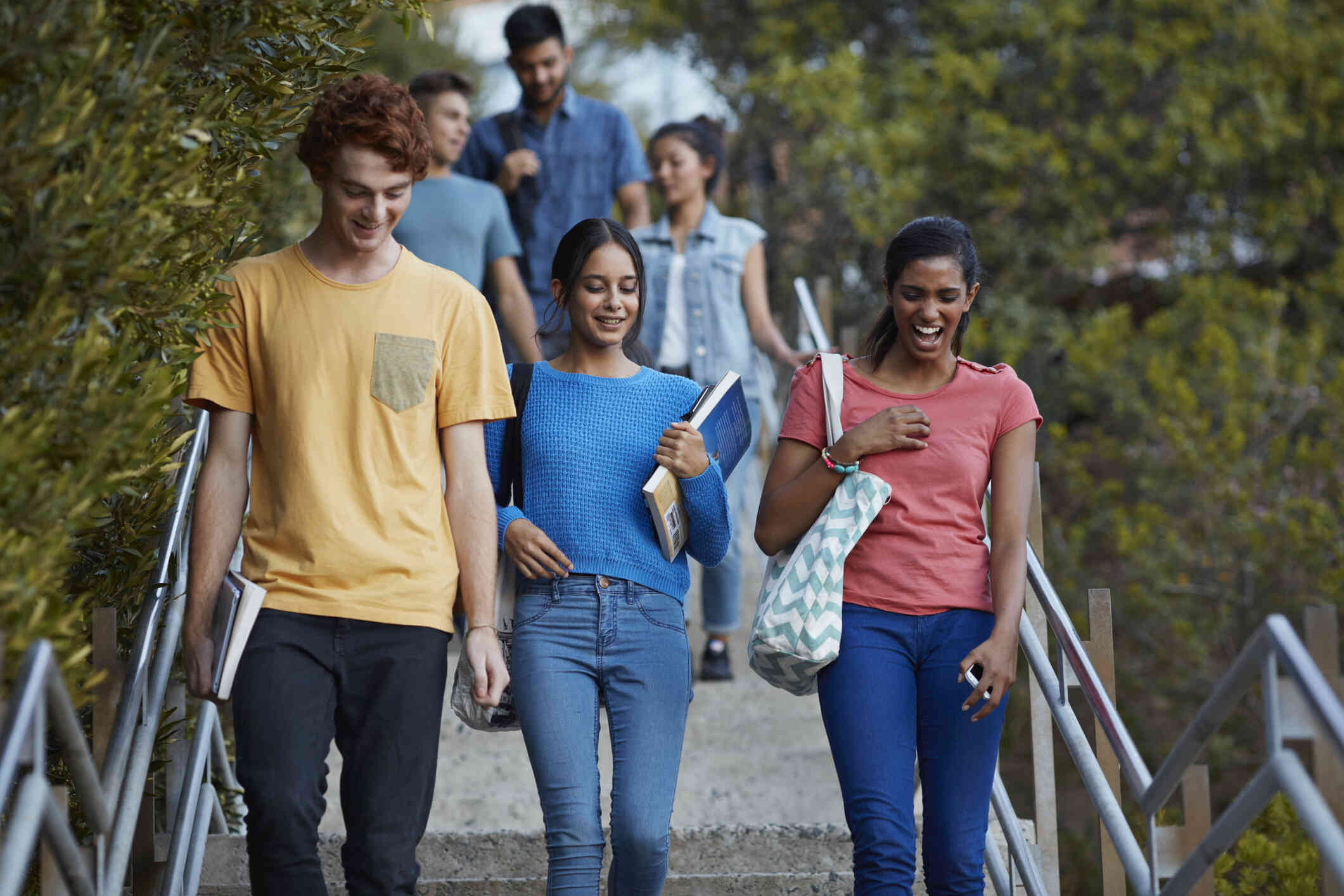 A group of teenagers walk together down a flight of outdoor steps on a sunny day while smiling and chatting.