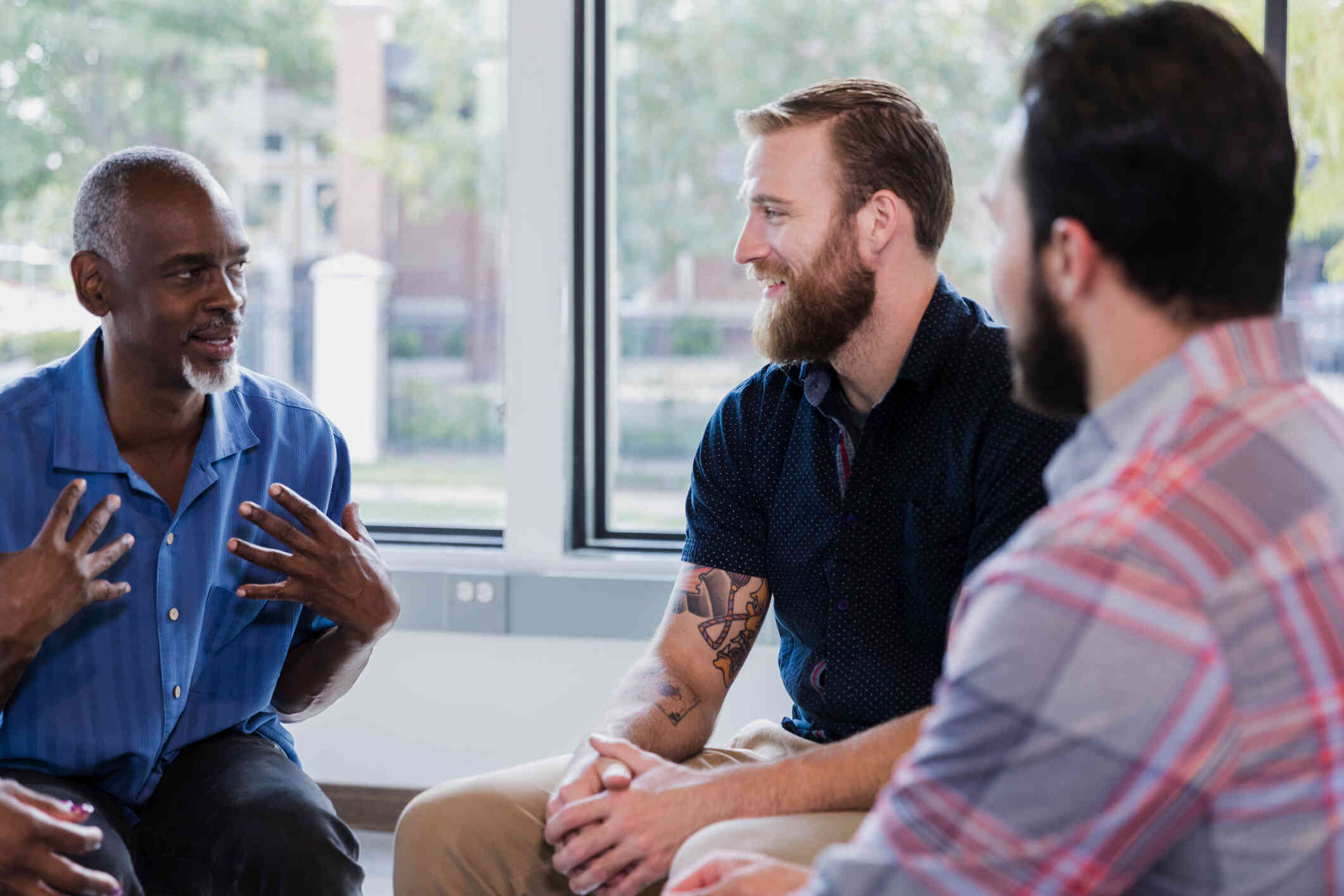 A group of men sit together in a circle and talk during a group therapy session.