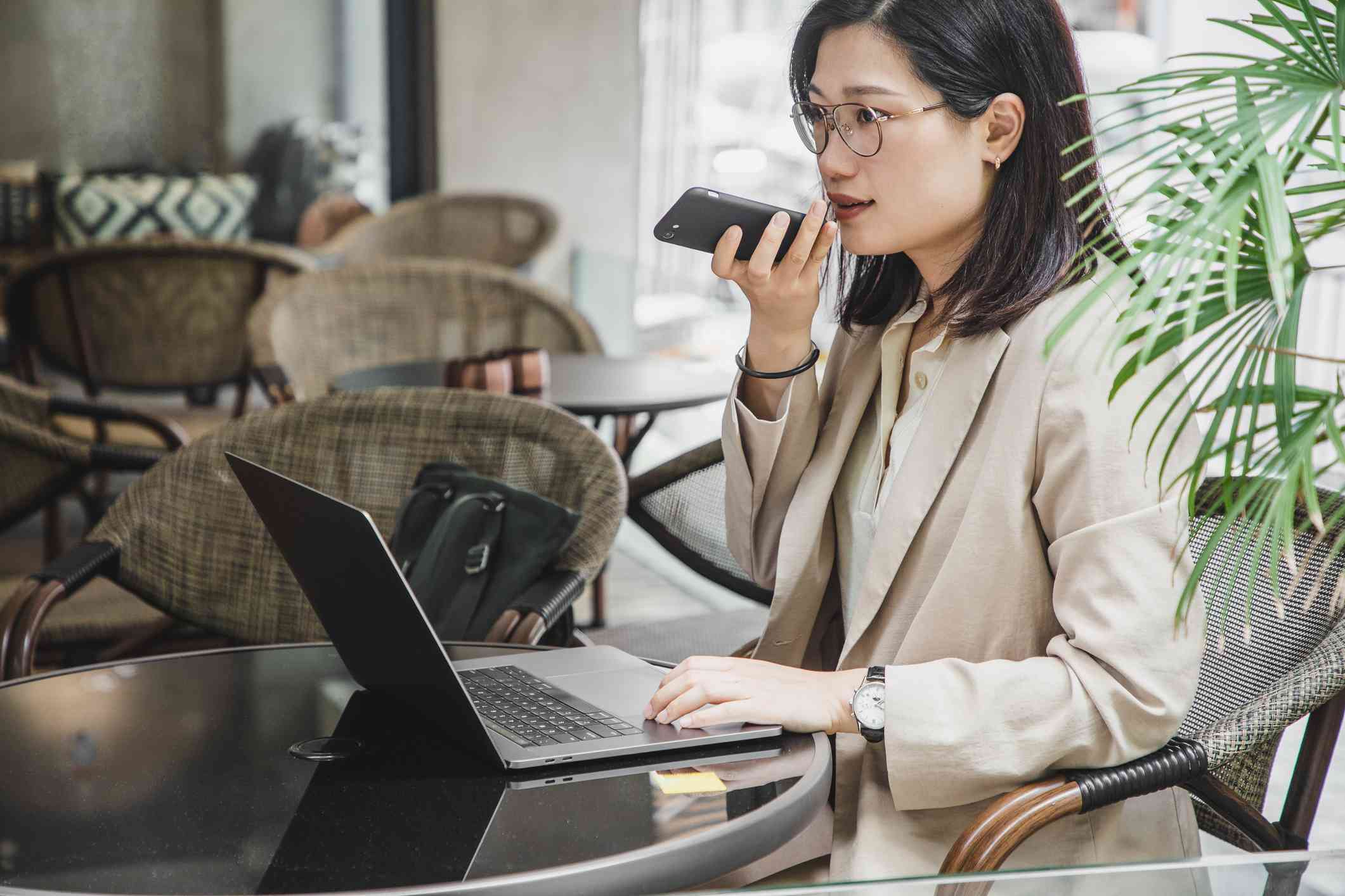 A female mental health professional sits outside at a table with her laptop open infront of her as she talks on the phone with a serious expression.