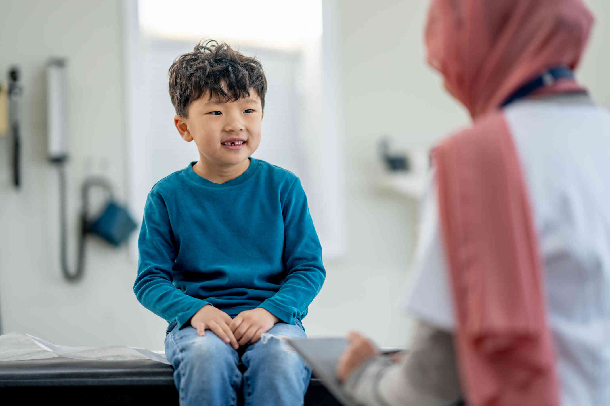 A young boy in a blue shirt smiles while sitting across from his female therapist during a therapy session.