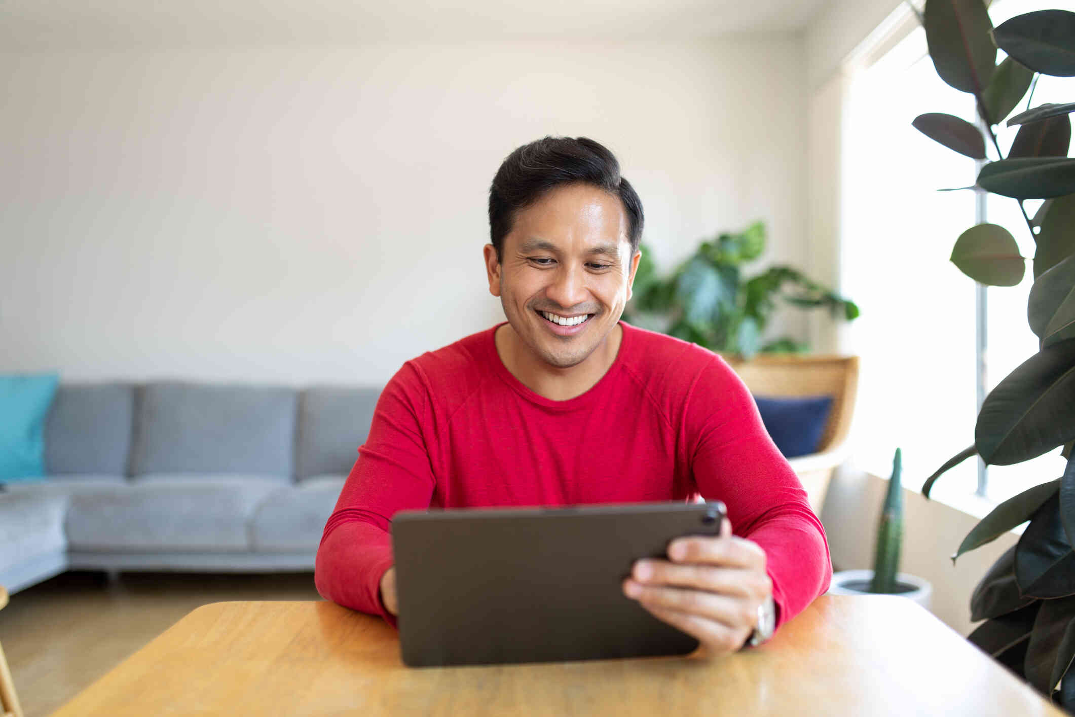 A man smiling at his laptop screen while seated at a table.