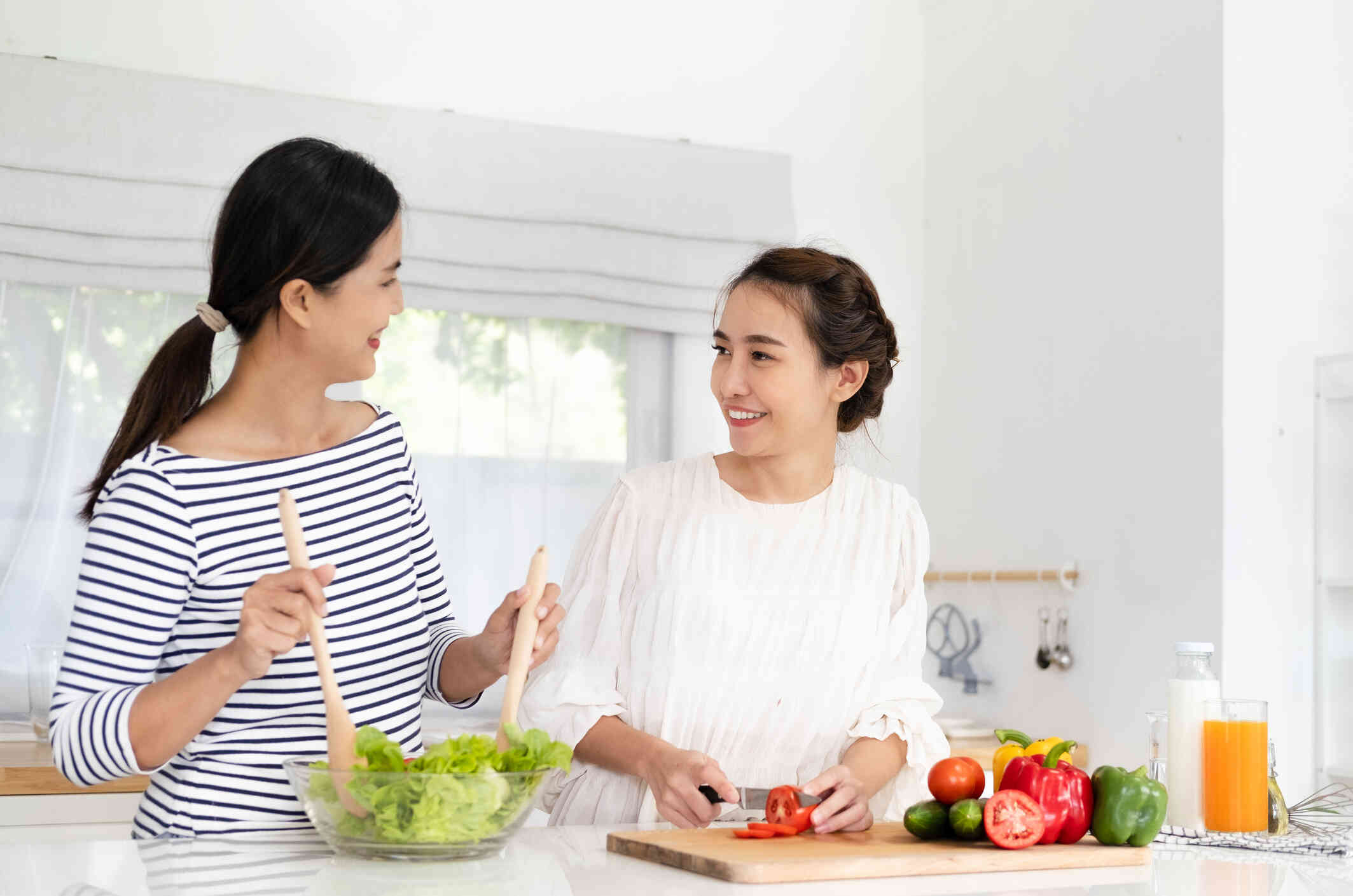 Two women stand side by side in the kitchen while cooking together and having a conversation.