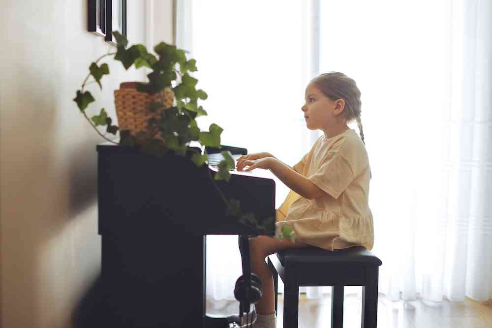 A young girl in a yellow dress sits at a baby-grand paino and practices her piano lessons. 