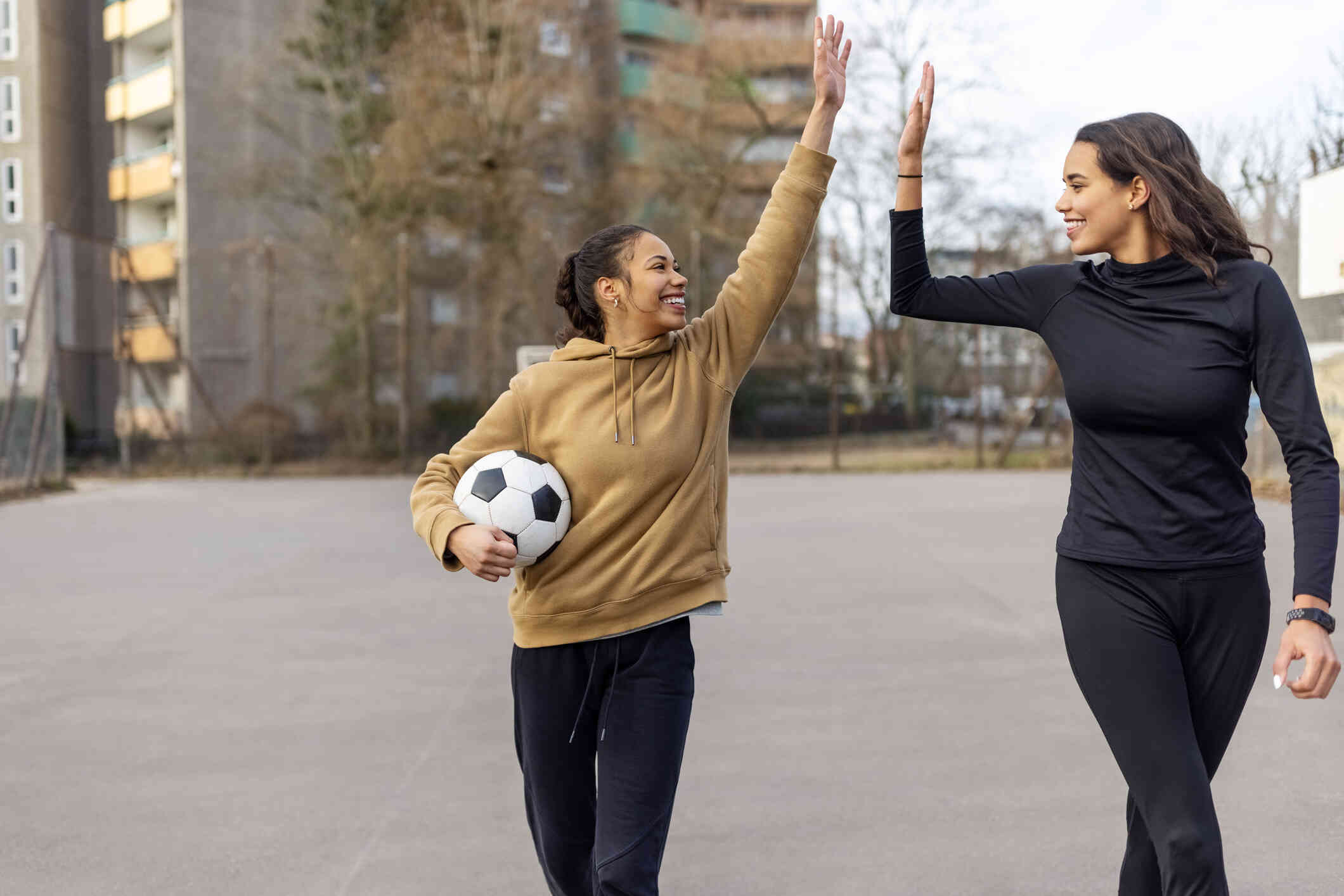 A woman holds a soccer ball while high fiving her friend who is walking next to her with a smile.