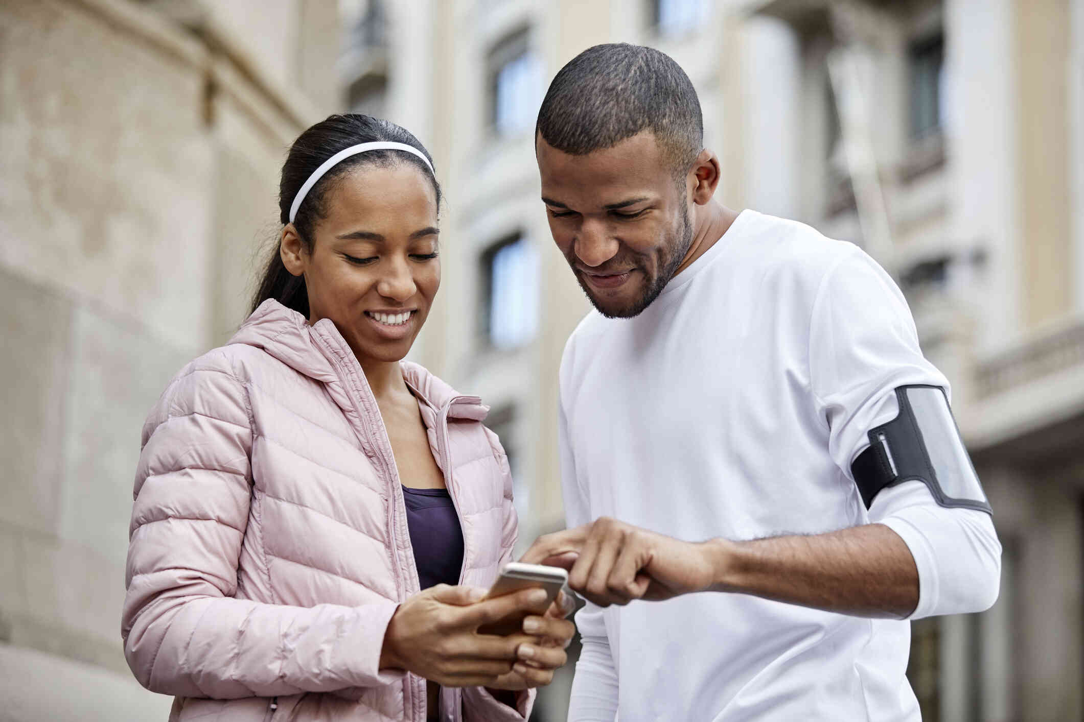 A man and woman stand outside on a sunny day and look at a phone together.