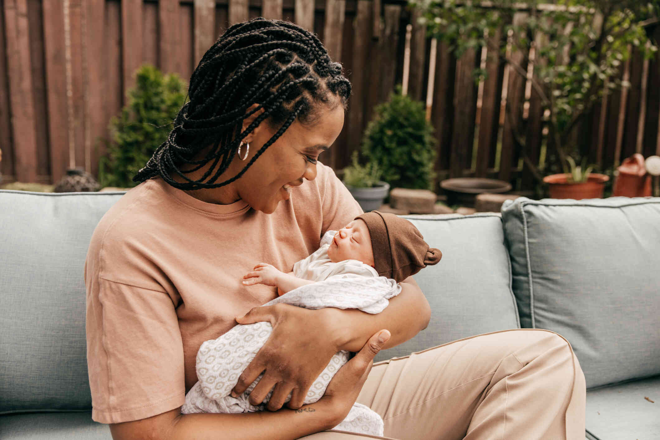 A woman sits outside while smiling and holding her newborn baby.