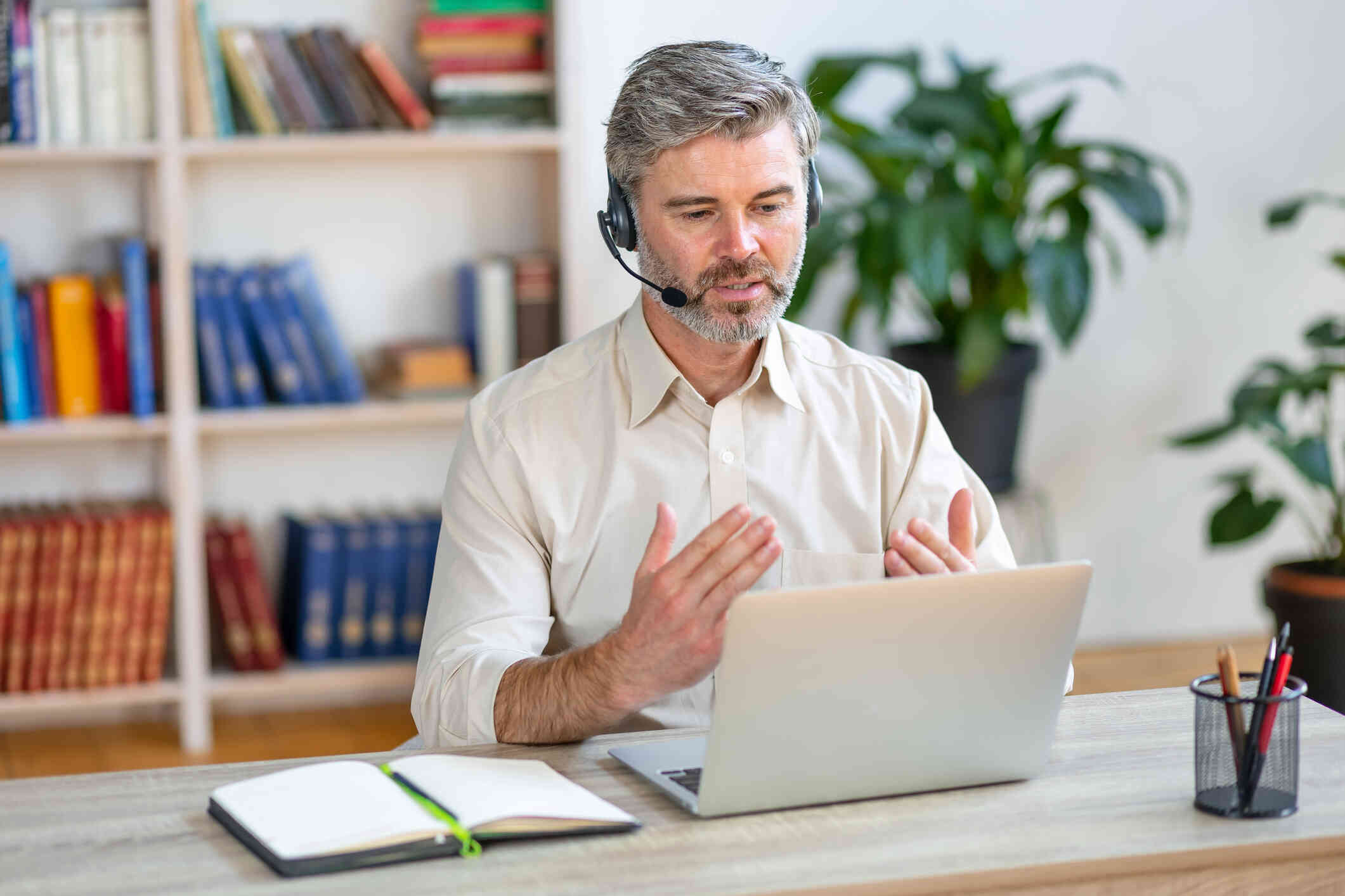 An older man in a polo with headphones on gestures while on a video call.