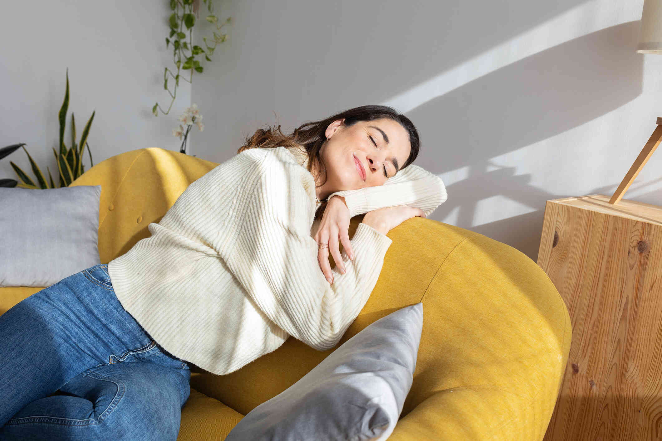 A women in a yellow shirt lays on a couch with her eyes closed with a content expressions