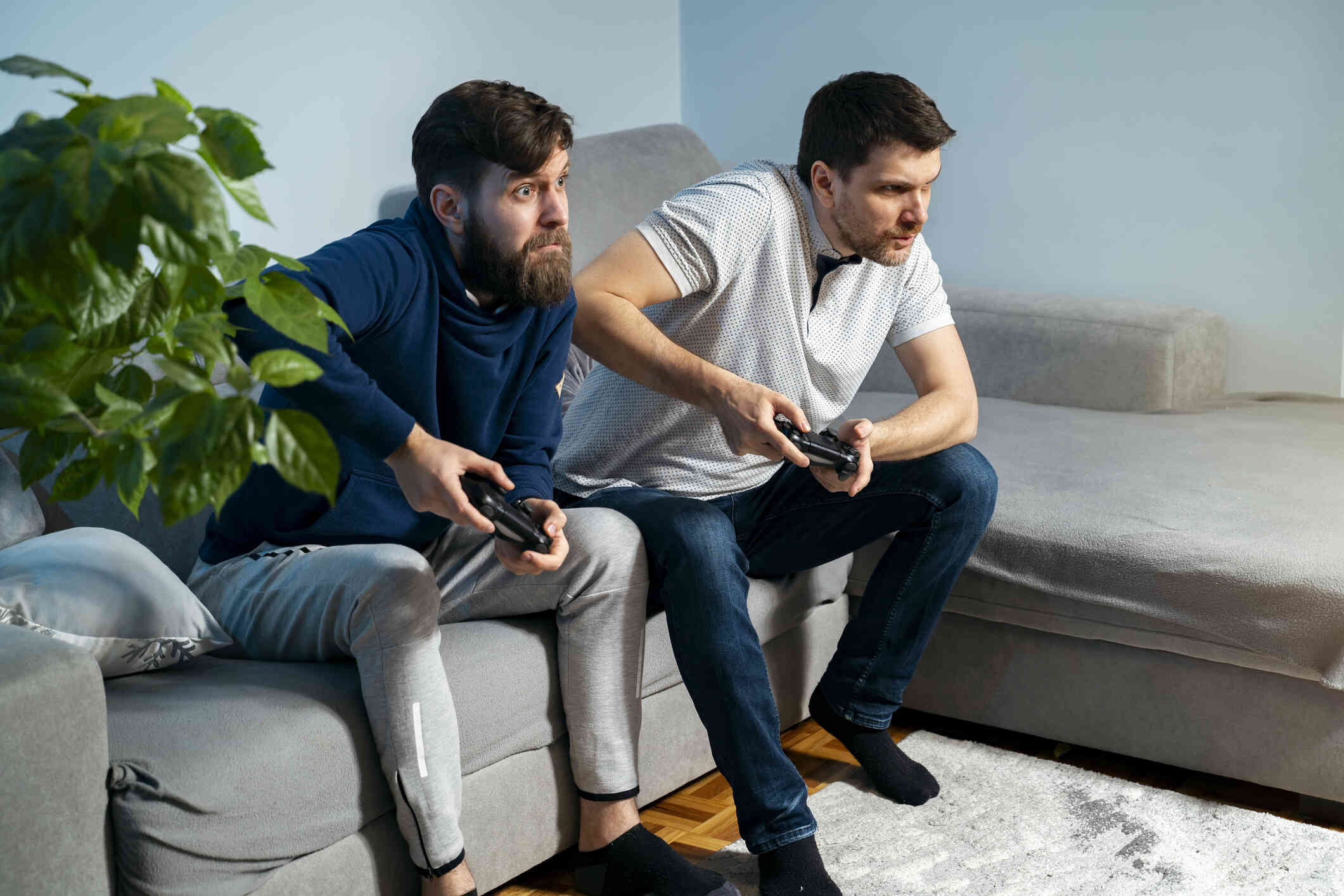 Two adult male friends sit side by side on the couch while playing video games together.