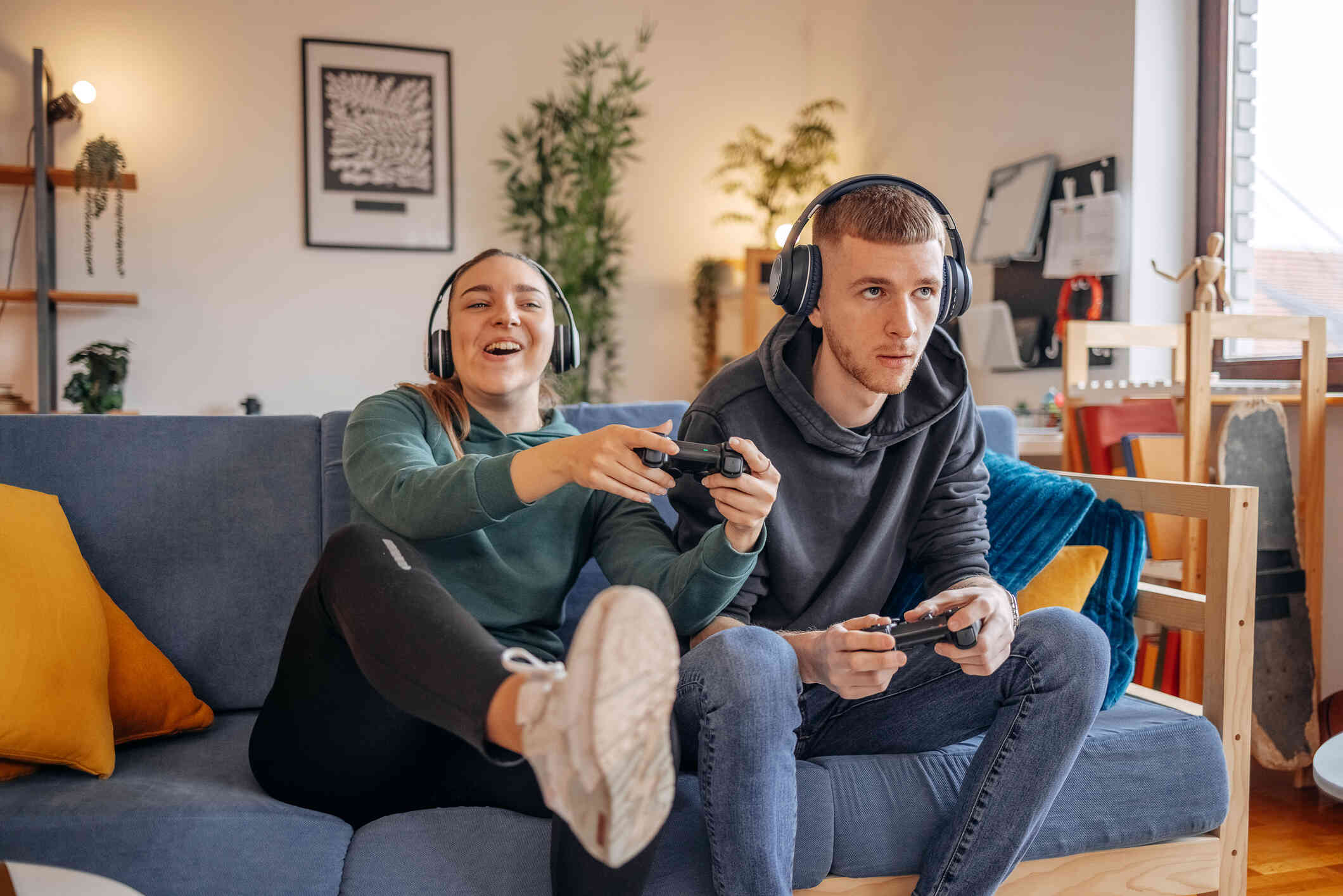 A woman and her male friend sit next to each other on the couch while playing video games together.