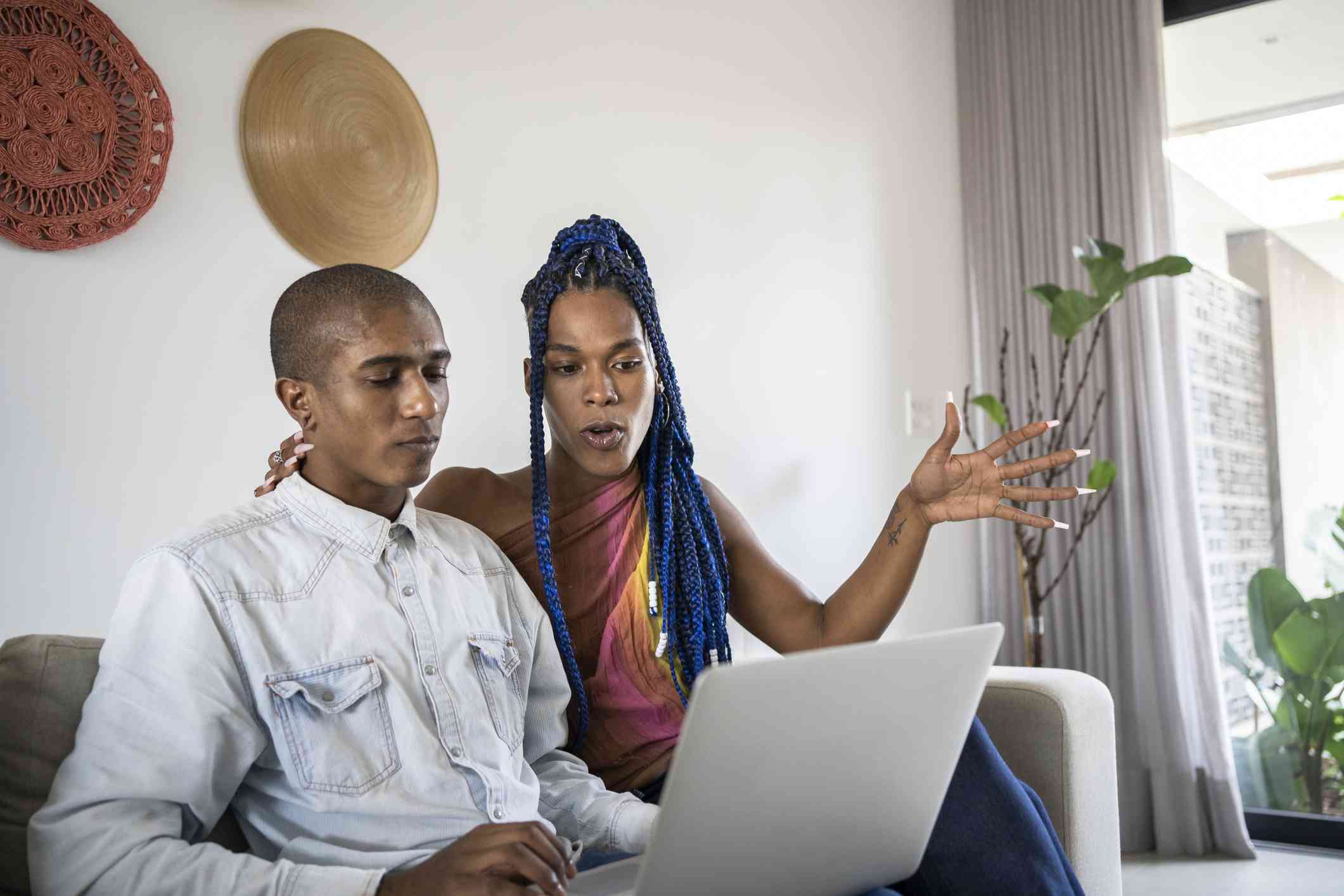 A couple is discussing something on their laptop while seated comfortably on their couch.