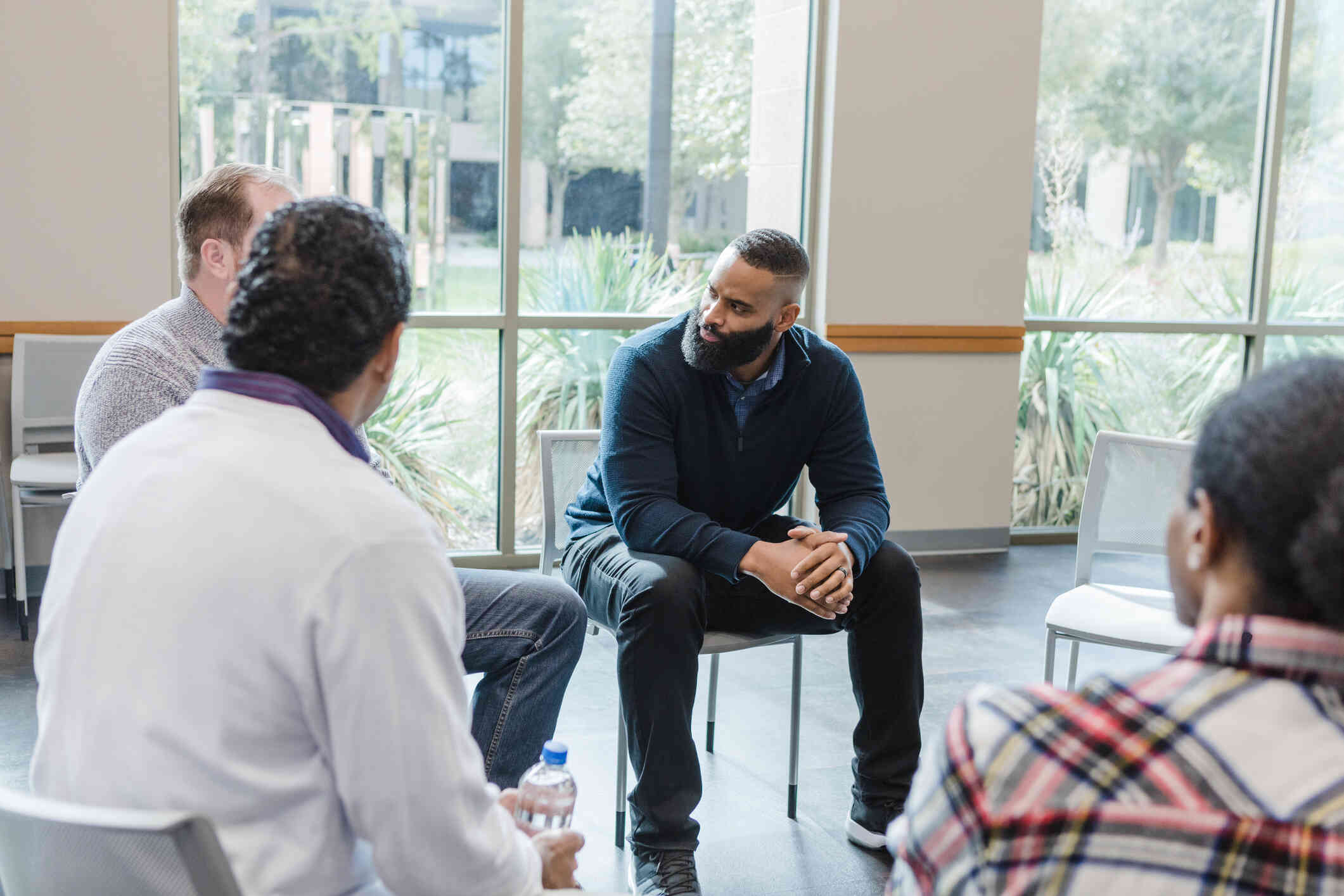 A group of adults sit in a group therapy circle.