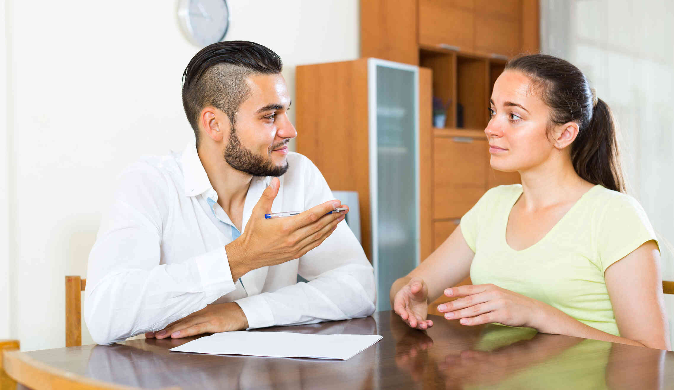 A male and female couple sit at the kitchen table and have a conversation.