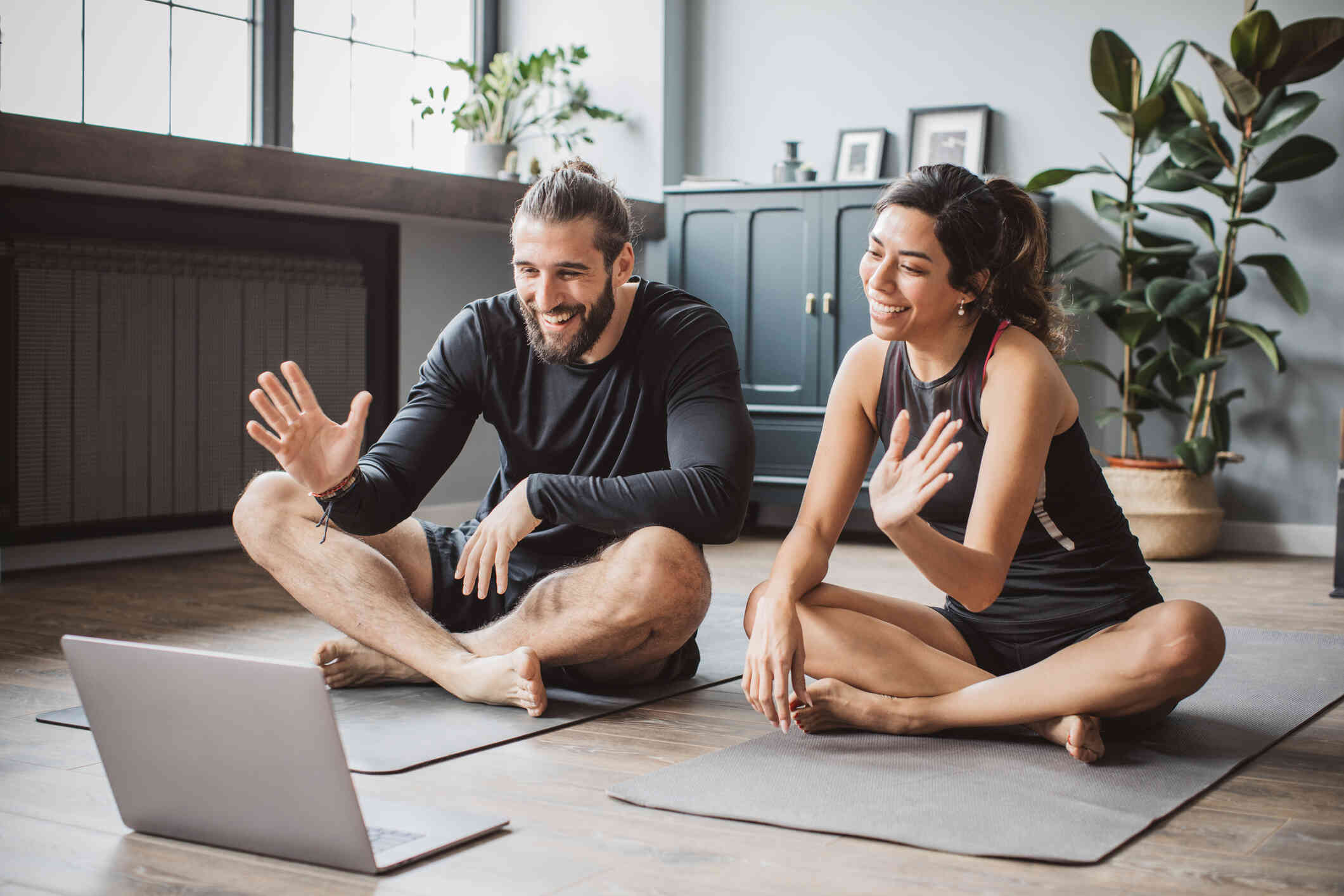 A couple sitting on their yoga mat, talking to someone on their laptop.