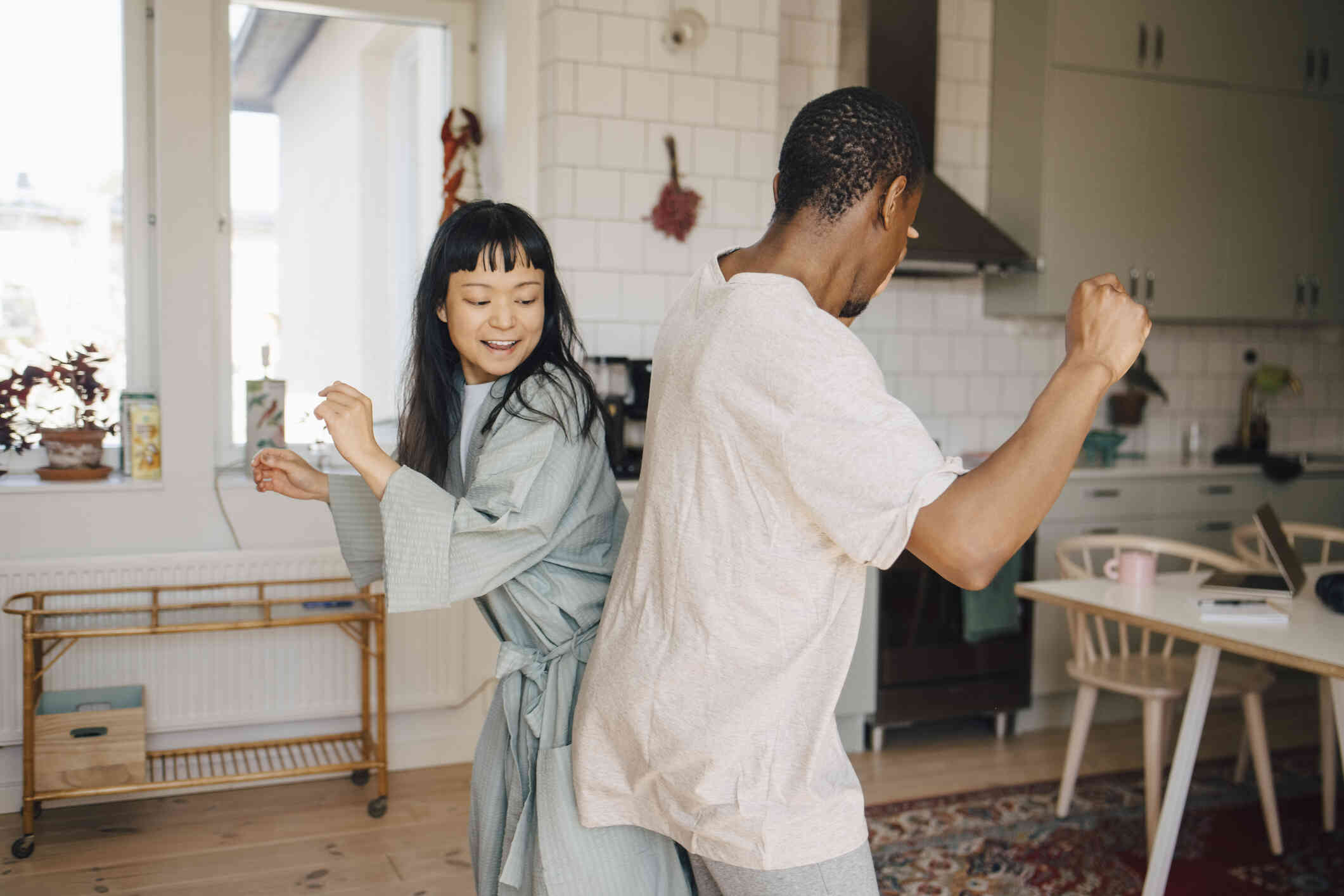 A male and female couple wearing pajamas dance together in their livingroom while smiling.