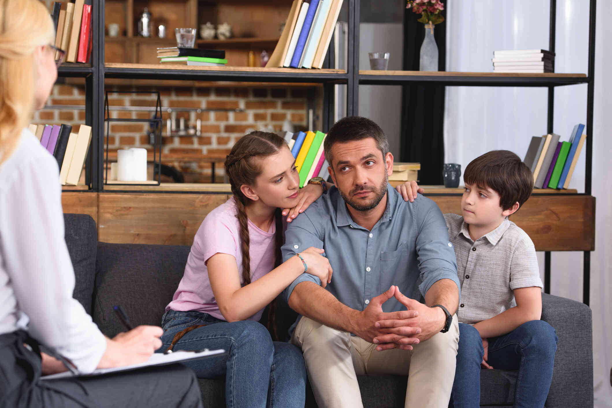 A man with his children beside him is sitting on couch across a female therapist.