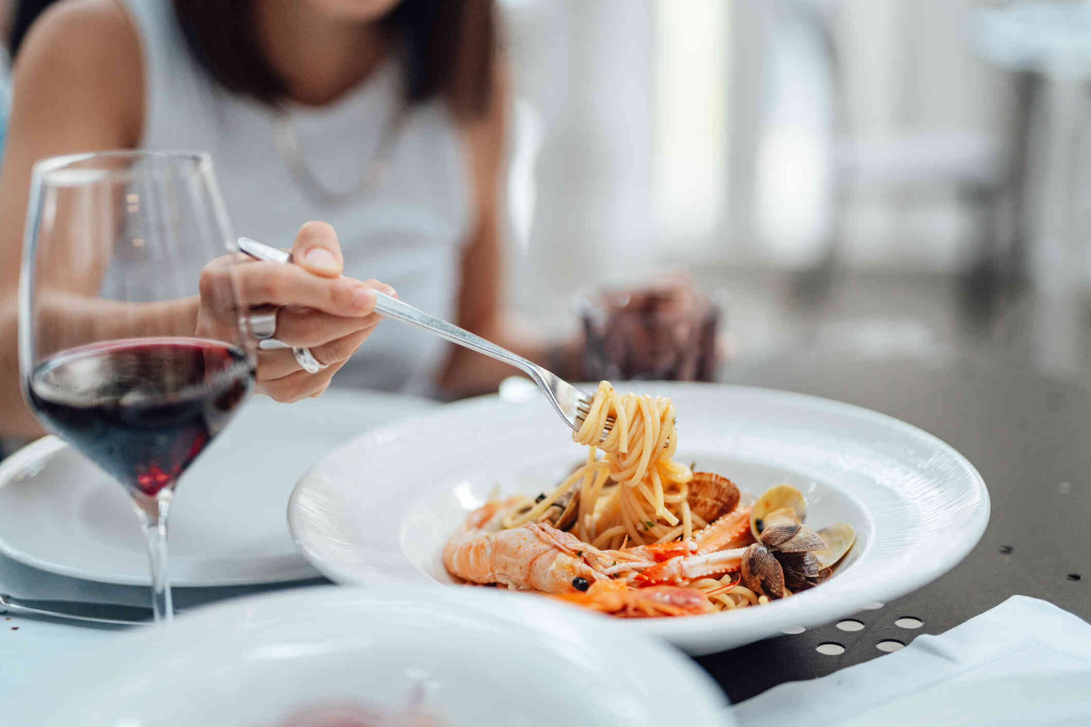 A close up of a woman twirling some pasta on her fork while sitting at a dinner table.