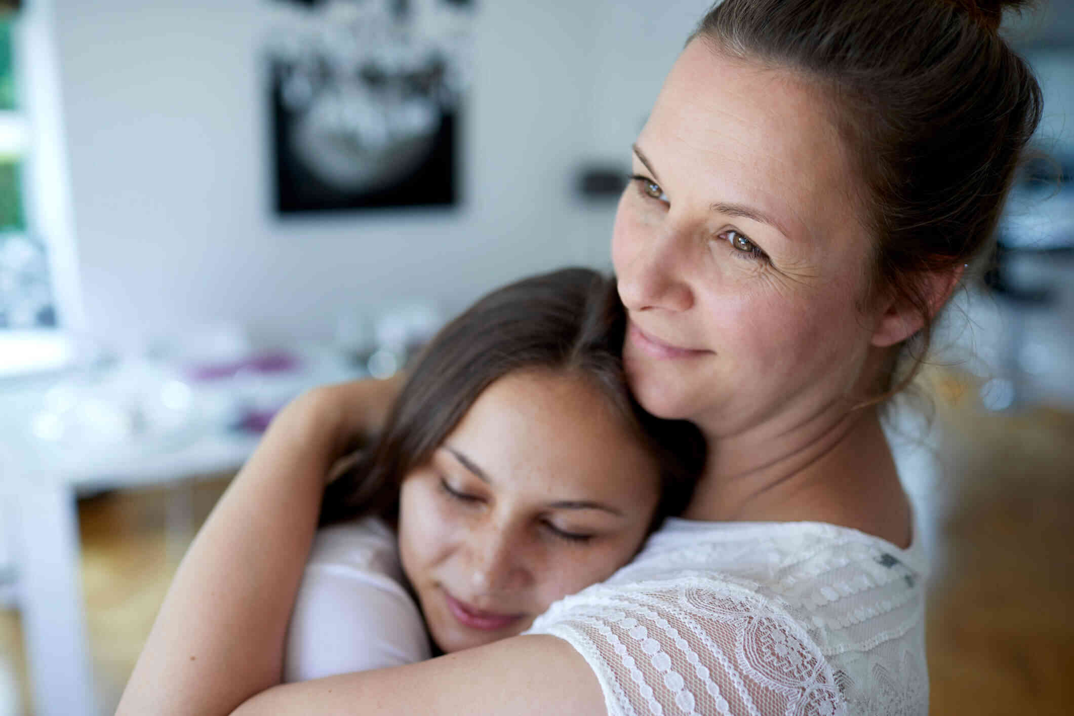 A close up of a daughter hugging her mother as the mother gazes off with a smile.