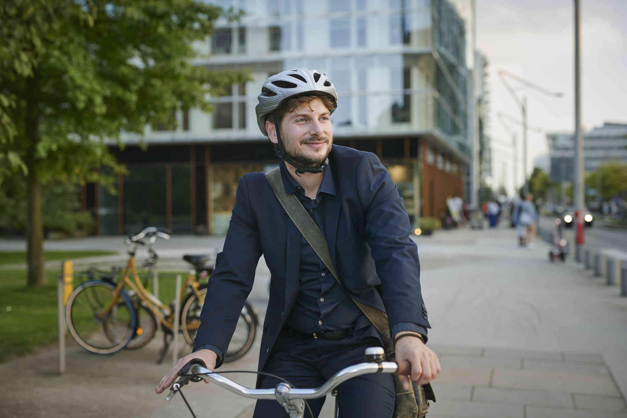 A man wearing a bicycle helmet and business attire smiles as he stands outside with his bike.